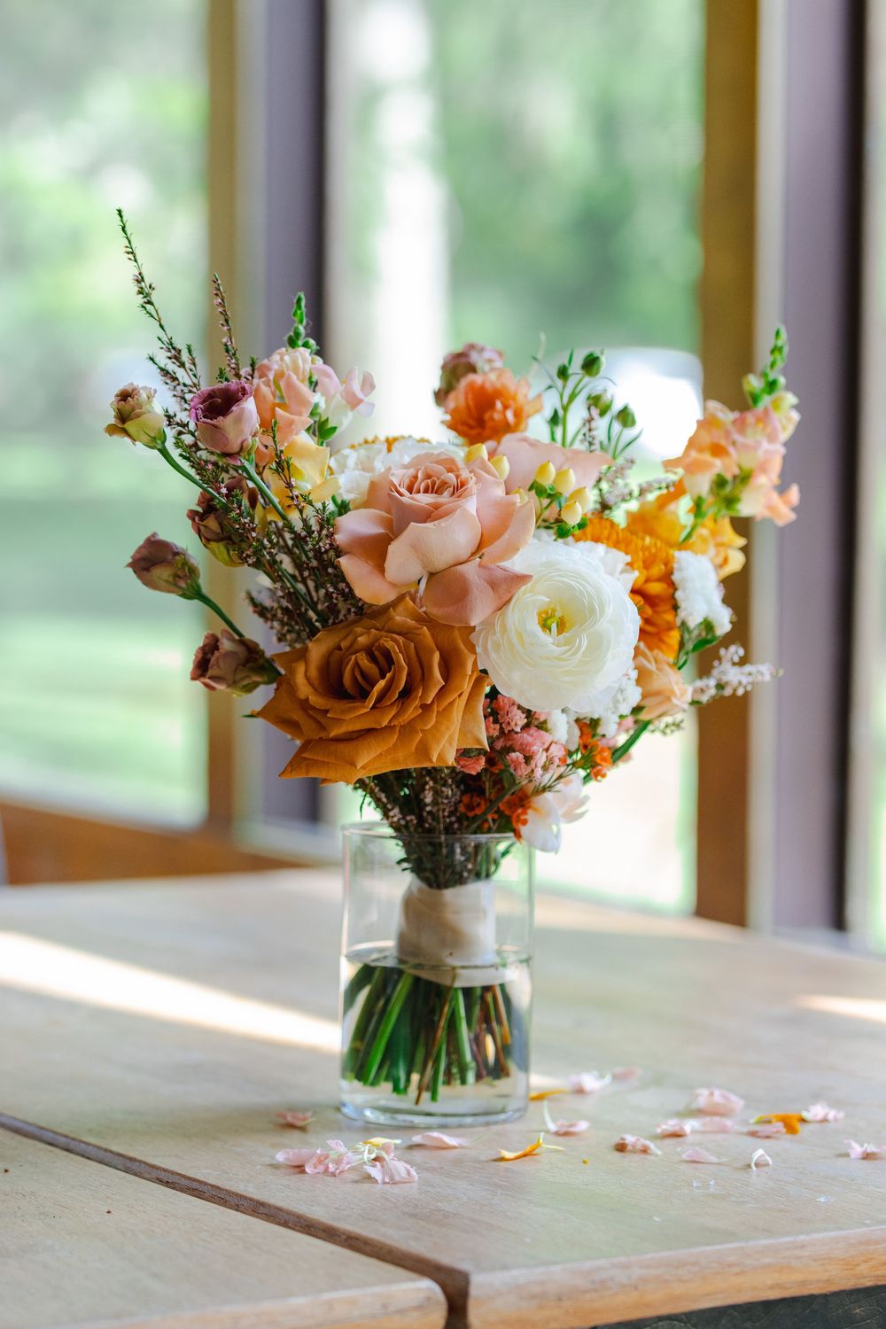 A bouquet of vibrant orange and white flowers, including roses and other blooms, displayed in a glass vase on a wooden table.