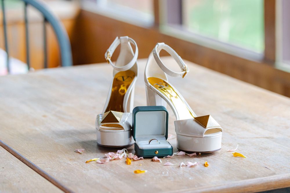 The image shows a pair of white high-heeled shoes, a jewelry box, and scattered jewelry on a wooden table.