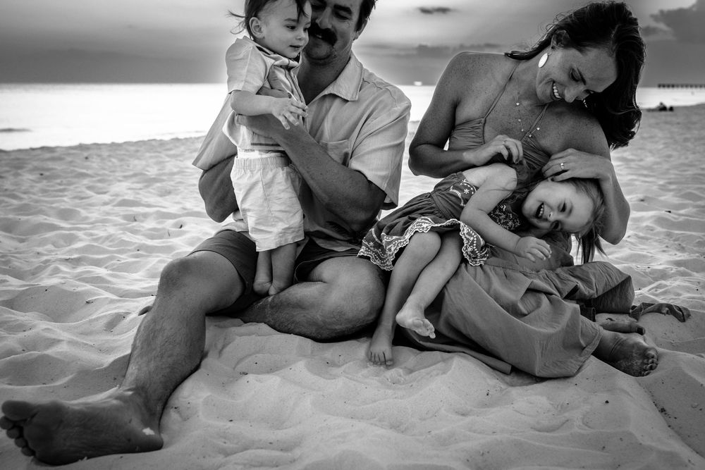 Black and white photo series showing intimate moments between parent and child playing on a beach at sunset.