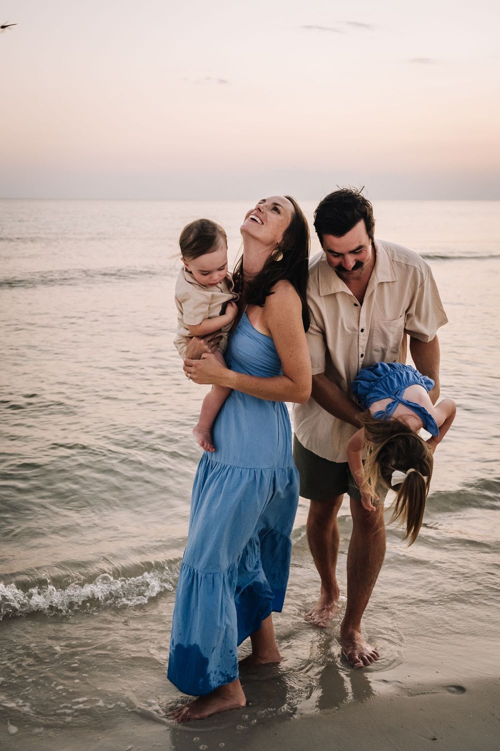 A family plays together in the ocean waves at sunset, splashing and laughing along the shoreline.