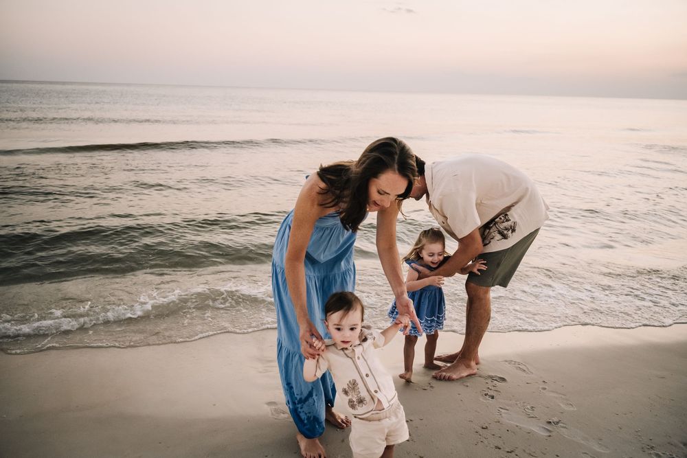 A couple in casual attire explores a sandy beach at sunset while waves gently roll in from the ocean.