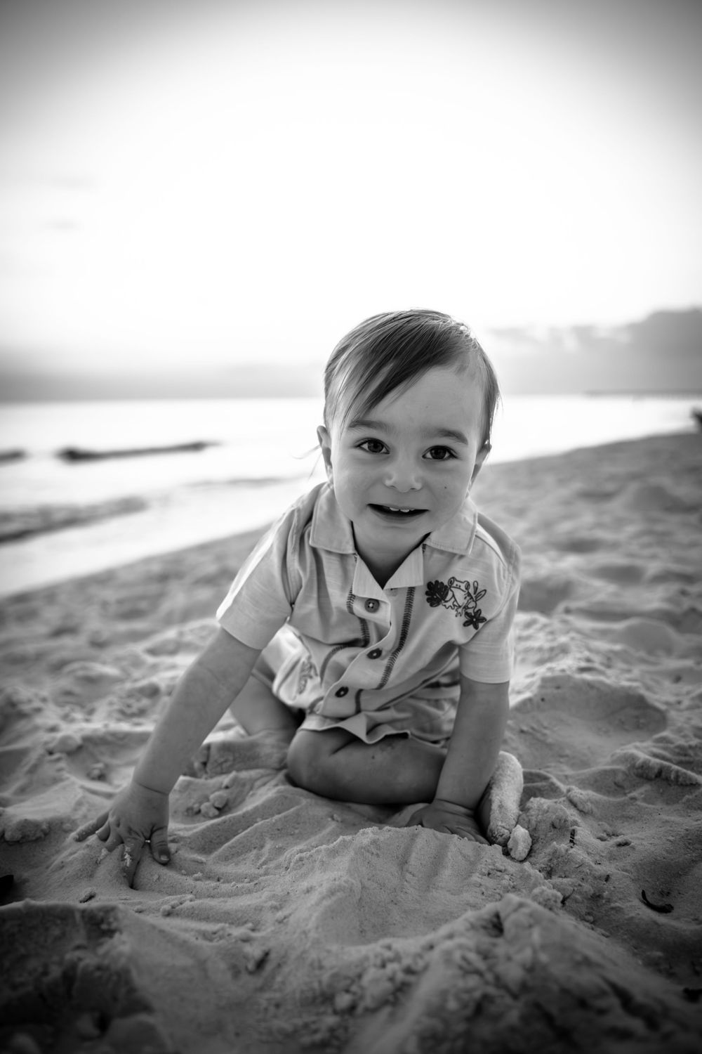 A sequence of black and white photos showing a baby crawling and playing on sandy beach.