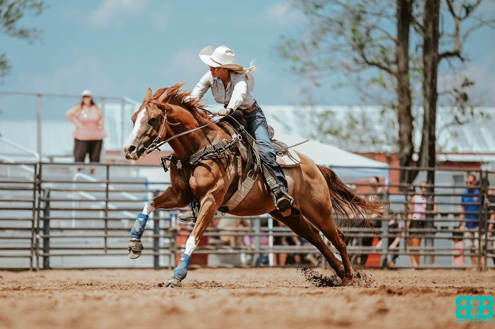 Western rider racing on chestnut horse in dusty arena during competition.