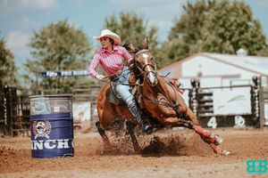 Barrel racing competitor making sharp turn around blue barrel in dusty arena.
