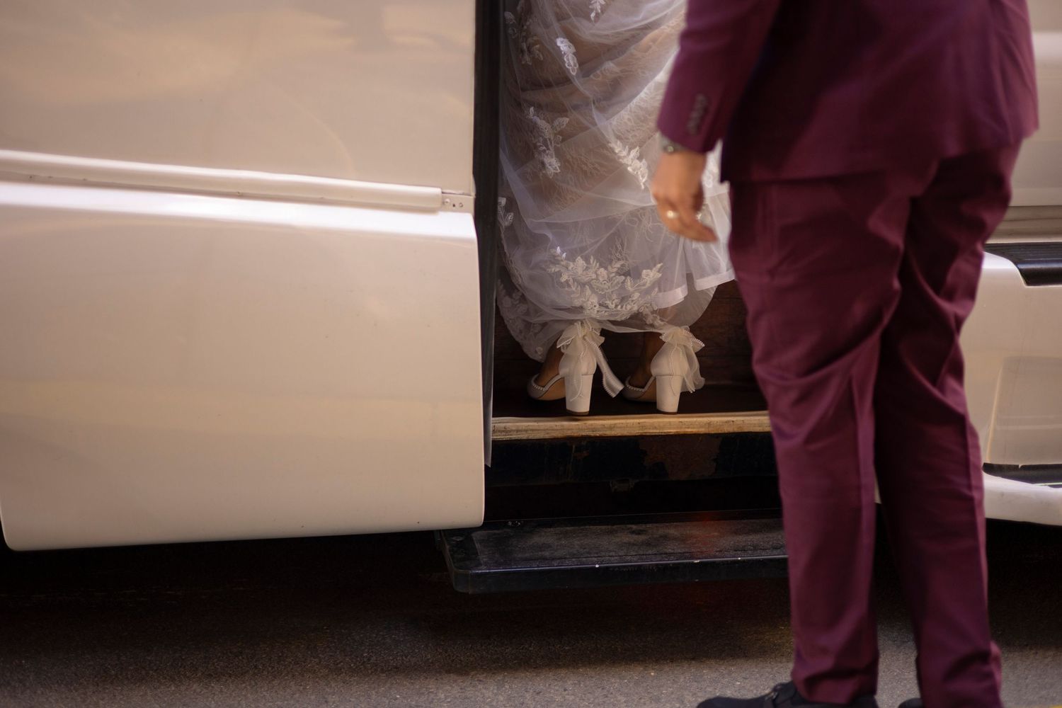 Bride and groom in a burgundy suit board a party bus to their wedding reception.
