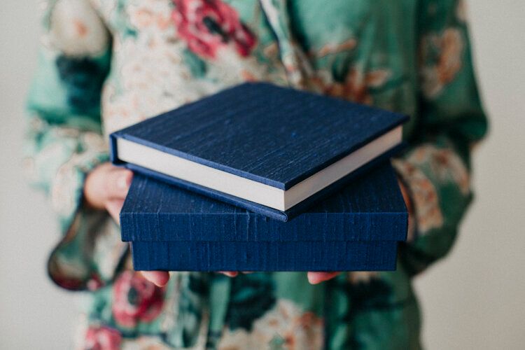 Hands holding two navy blue hardcover books while wearing a floral patterned green and pink dress.
