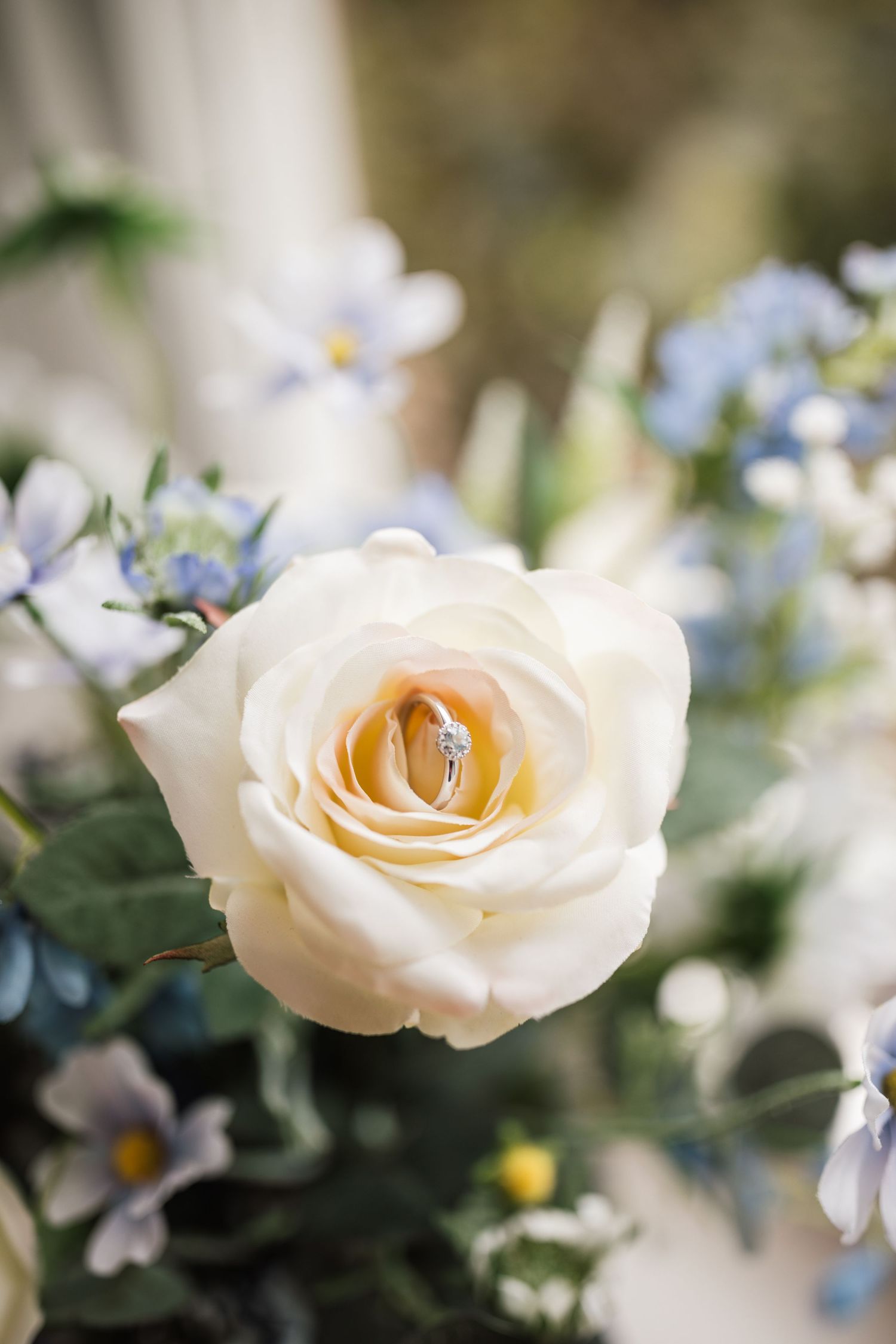 Close-up detail of cream and mauve roses with delicate blue flowers and eucalyptus leaves in a romantic floral arrangement.