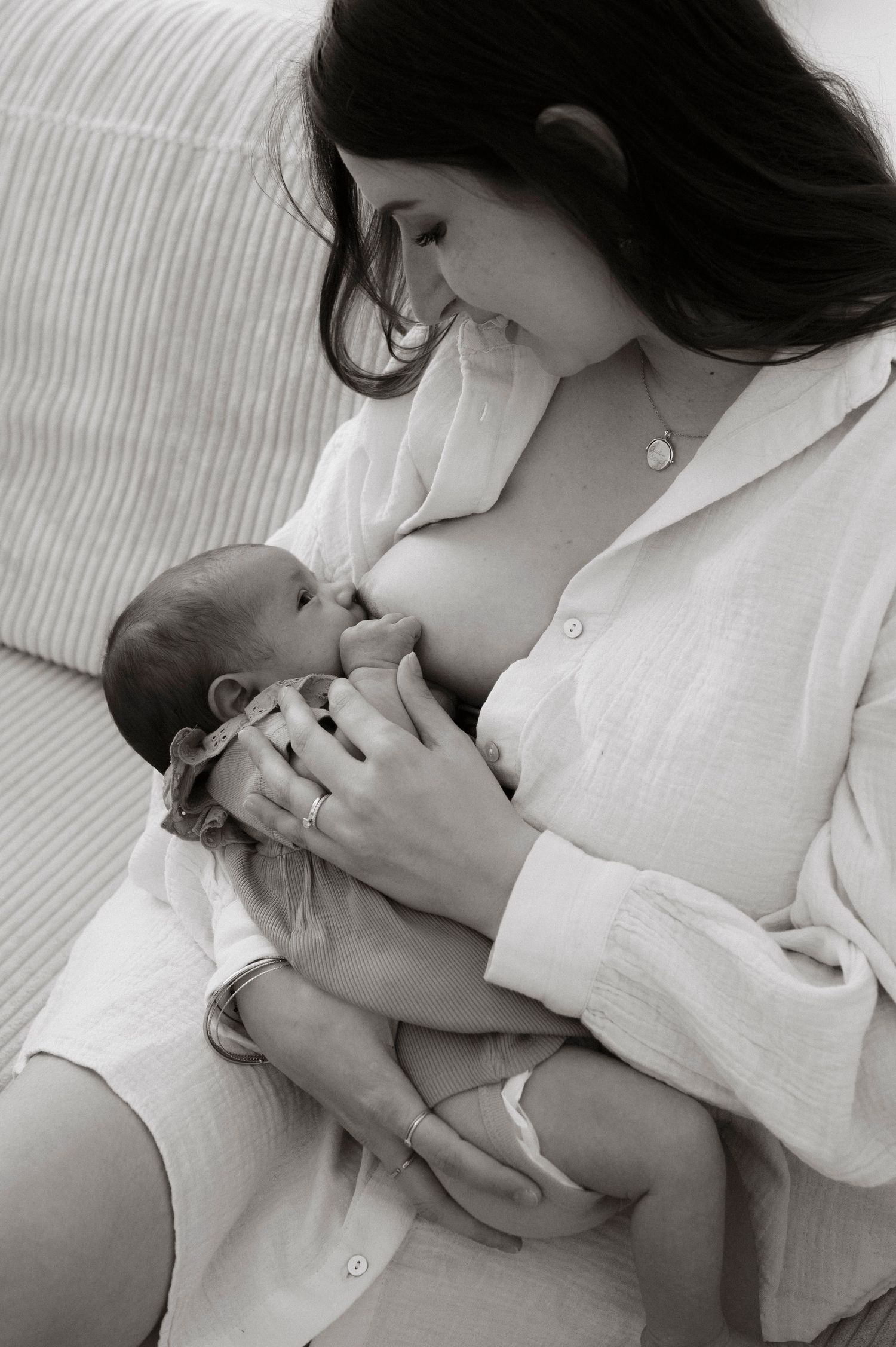 A tender black and white photograph shows a mother breastfeeding her newborn baby while wearing a white robe.