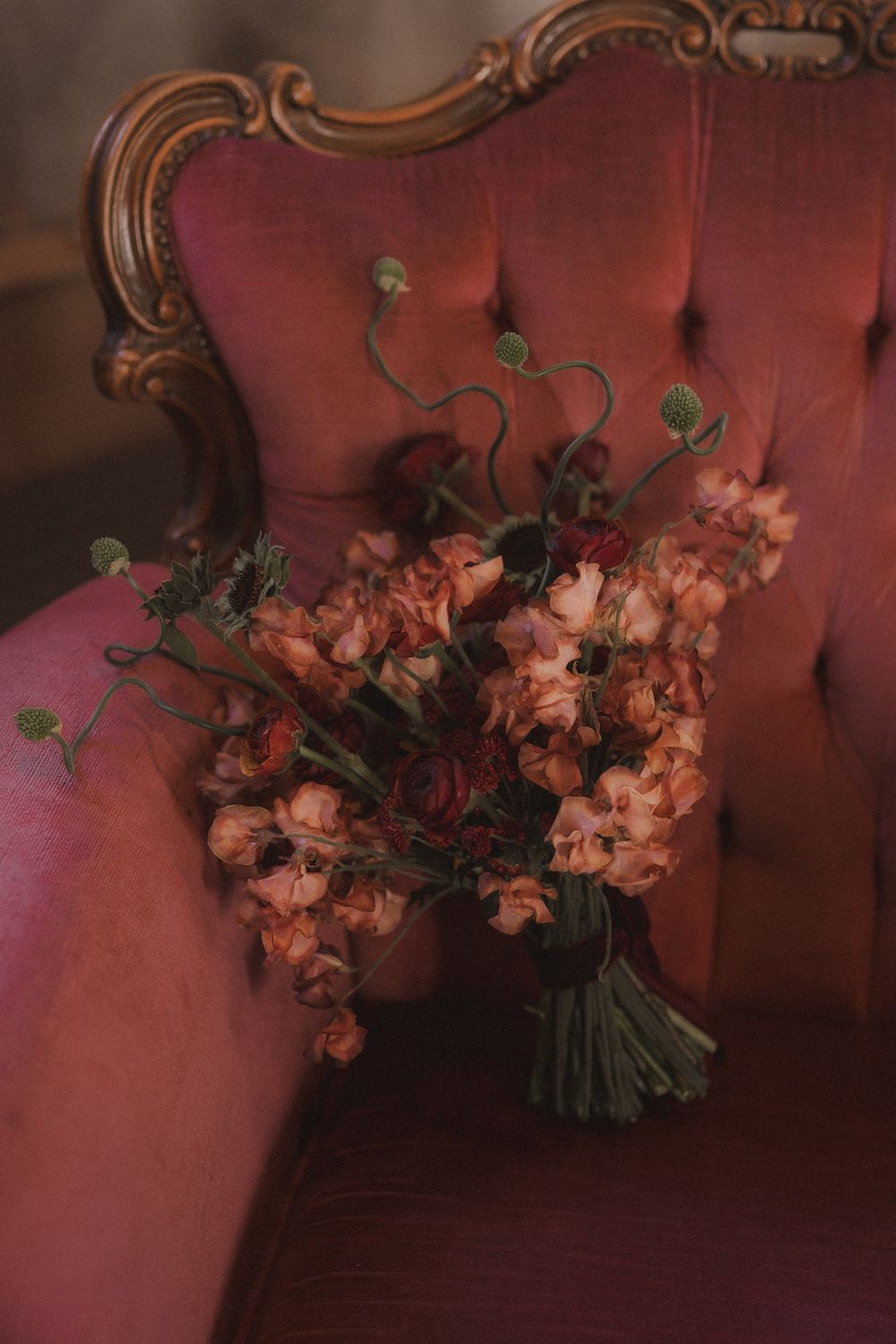 Pink and burgundy floral arrangement displayed on a vintage red velvet tufted sofa.