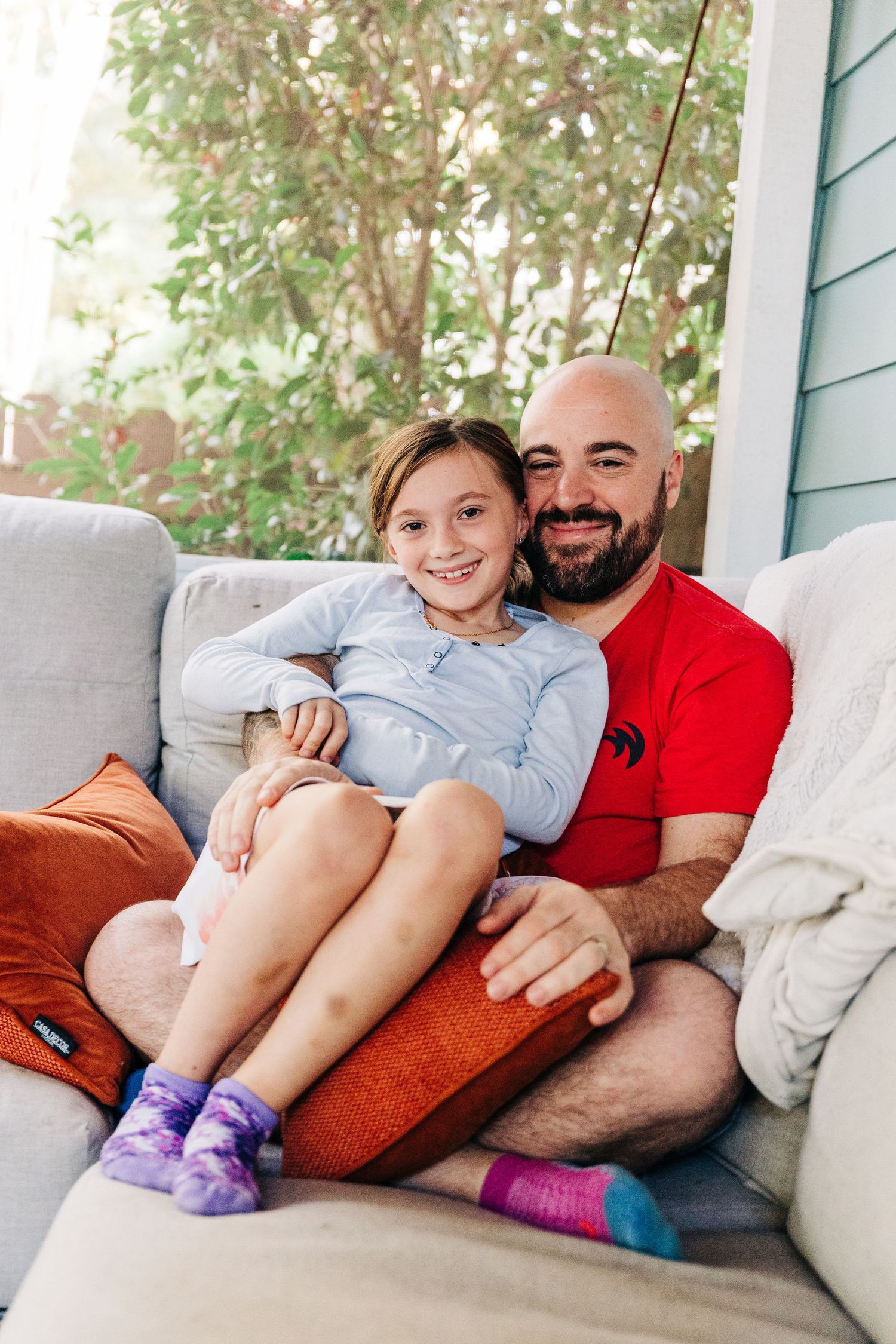 Father and daughter relax together on a comfortable gray couch while wearing colorful socks.