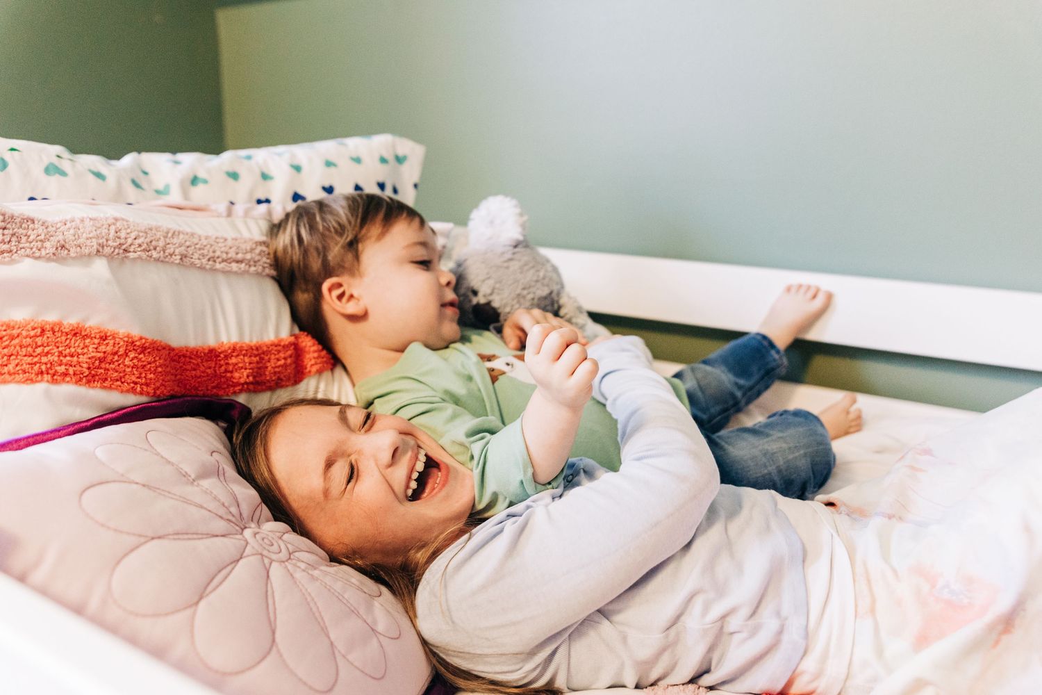 Siblings playing and laughing while laying on a bed during Charlotte photo session.