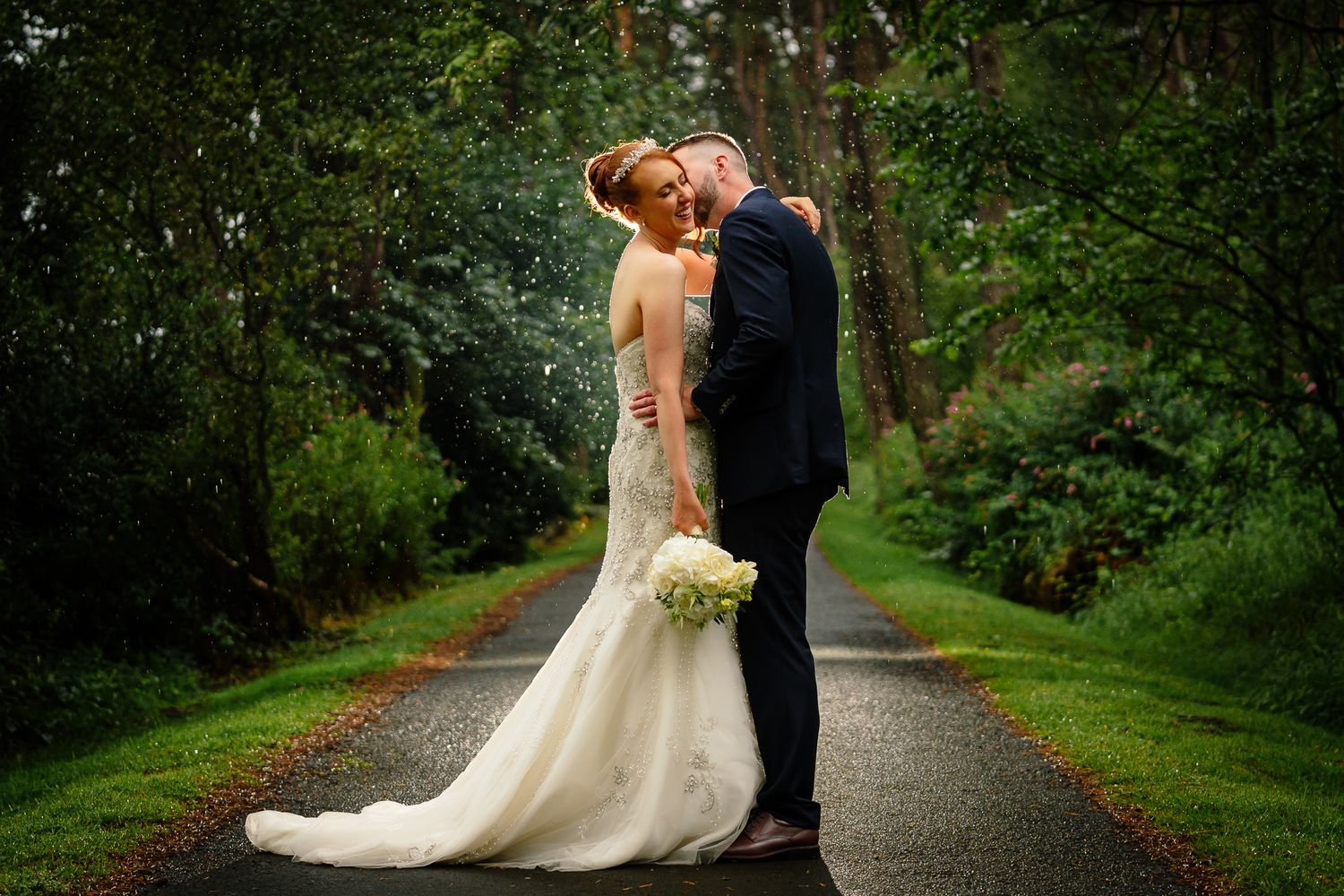 A couple shares an intimate moment on a tree-lined path during their wedding photoshoot. Woodhill Hall.