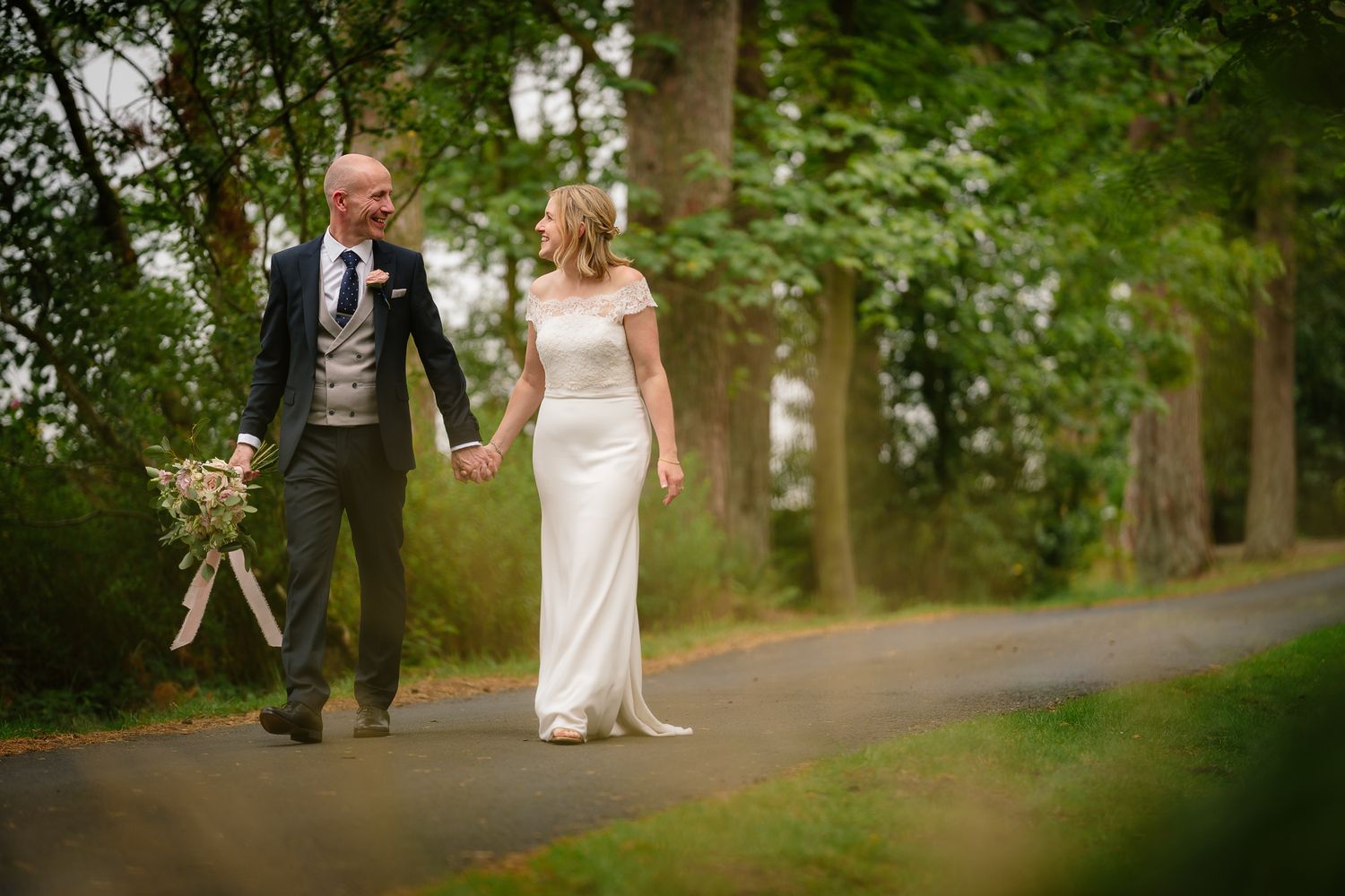 Wedding couple walking along a scenic tree-lined path during golden hour. Woodhill Hall.