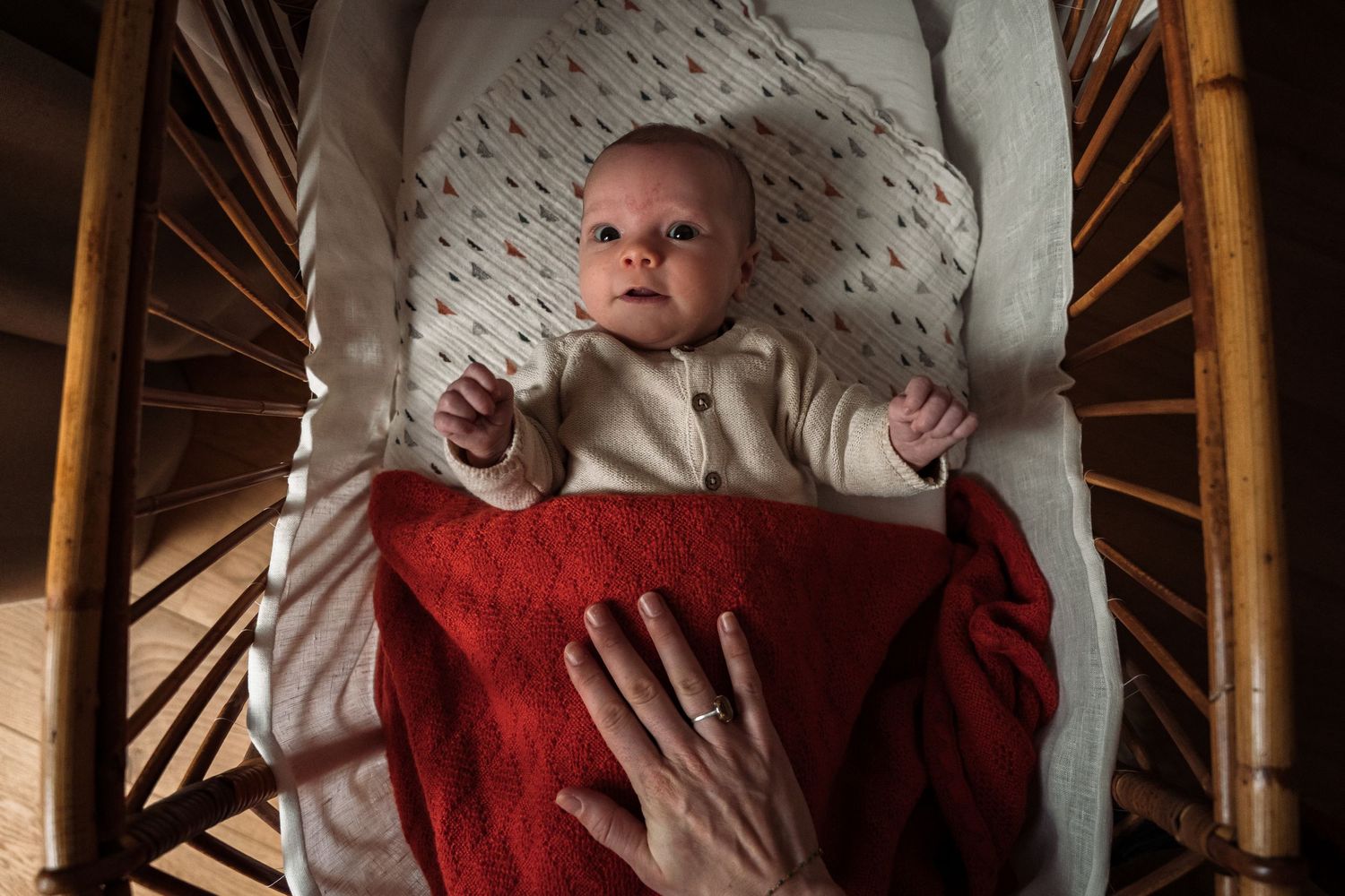 A newborn baby cries while being photographed through a narrow opening, creating a dramatic vignette effect.