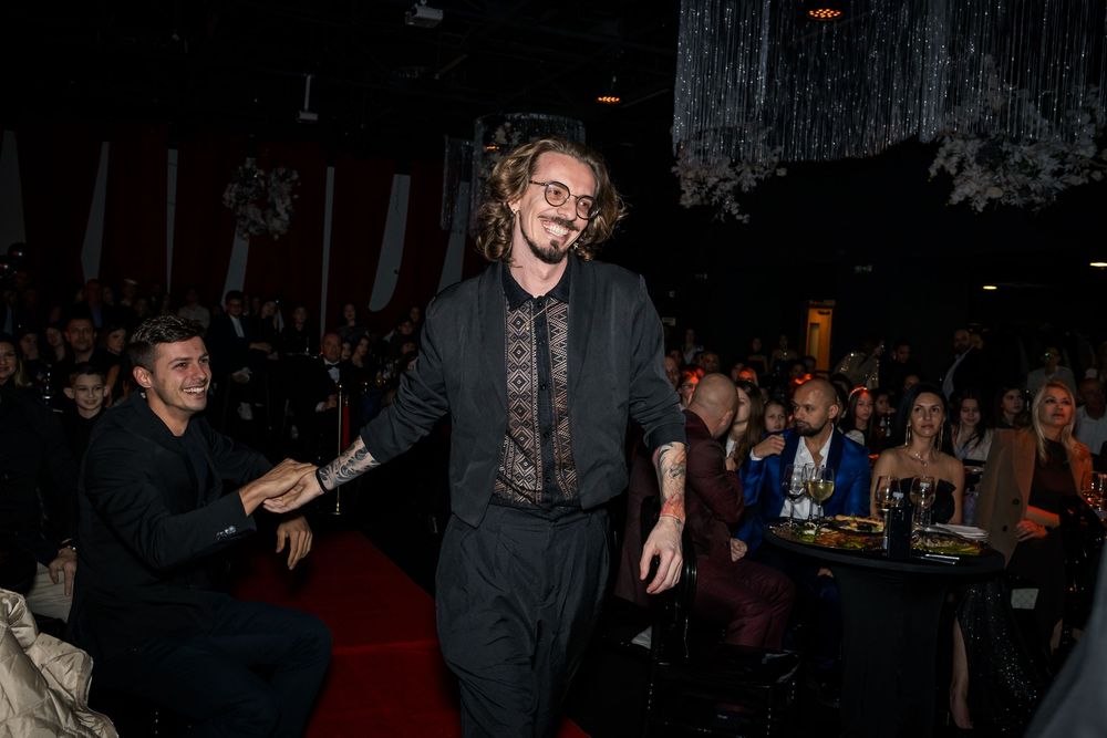 Man with dreadlocks in black outfit walking through crowded awards ceremony venue.