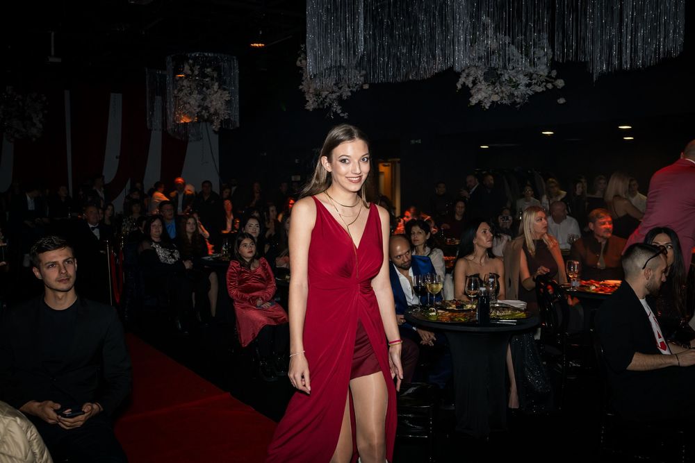 Woman in elegant red dress walks red carpet runway at glamorous evening gala event.