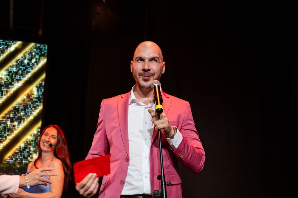 Bald man in pink blazer speaks into microphone on stage at awards ceremony.
