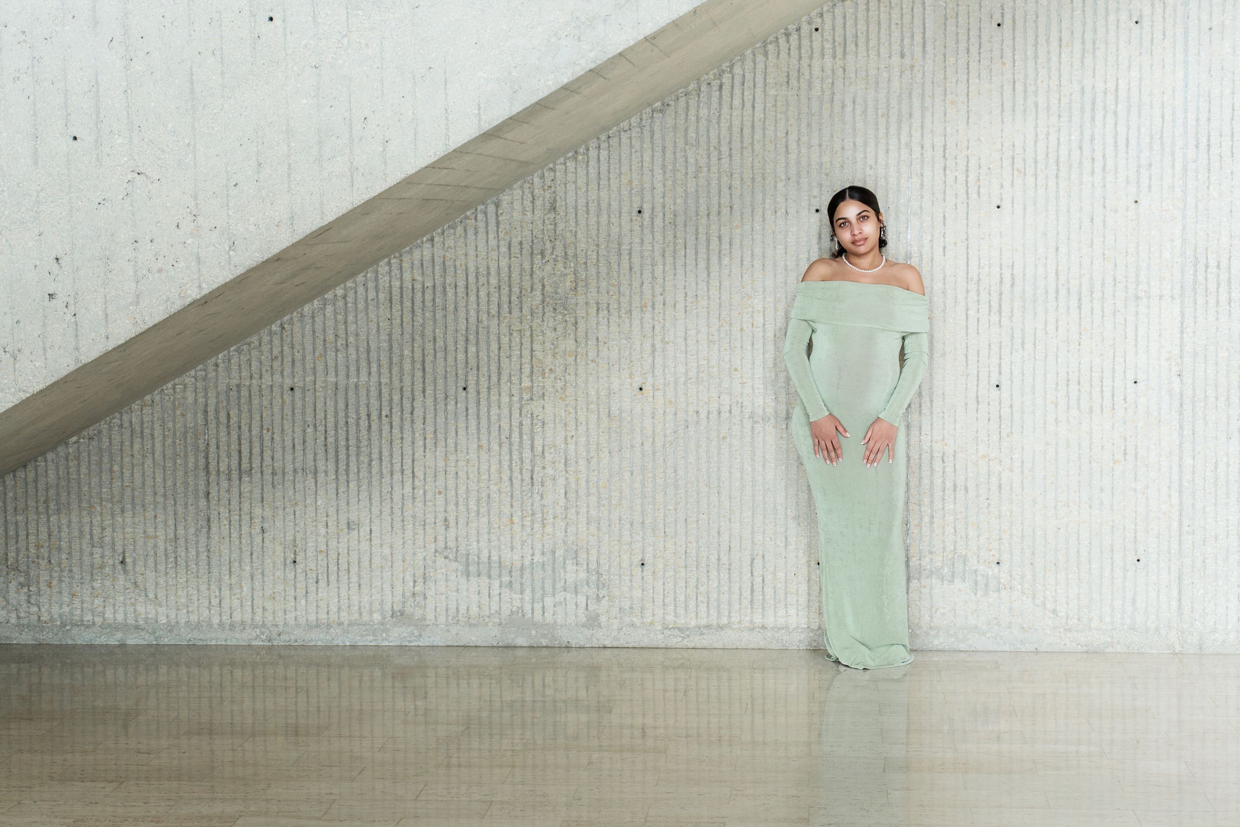 A model walks down a minimalist white runway wearing a flowing mint green evening gown in a fashion show.