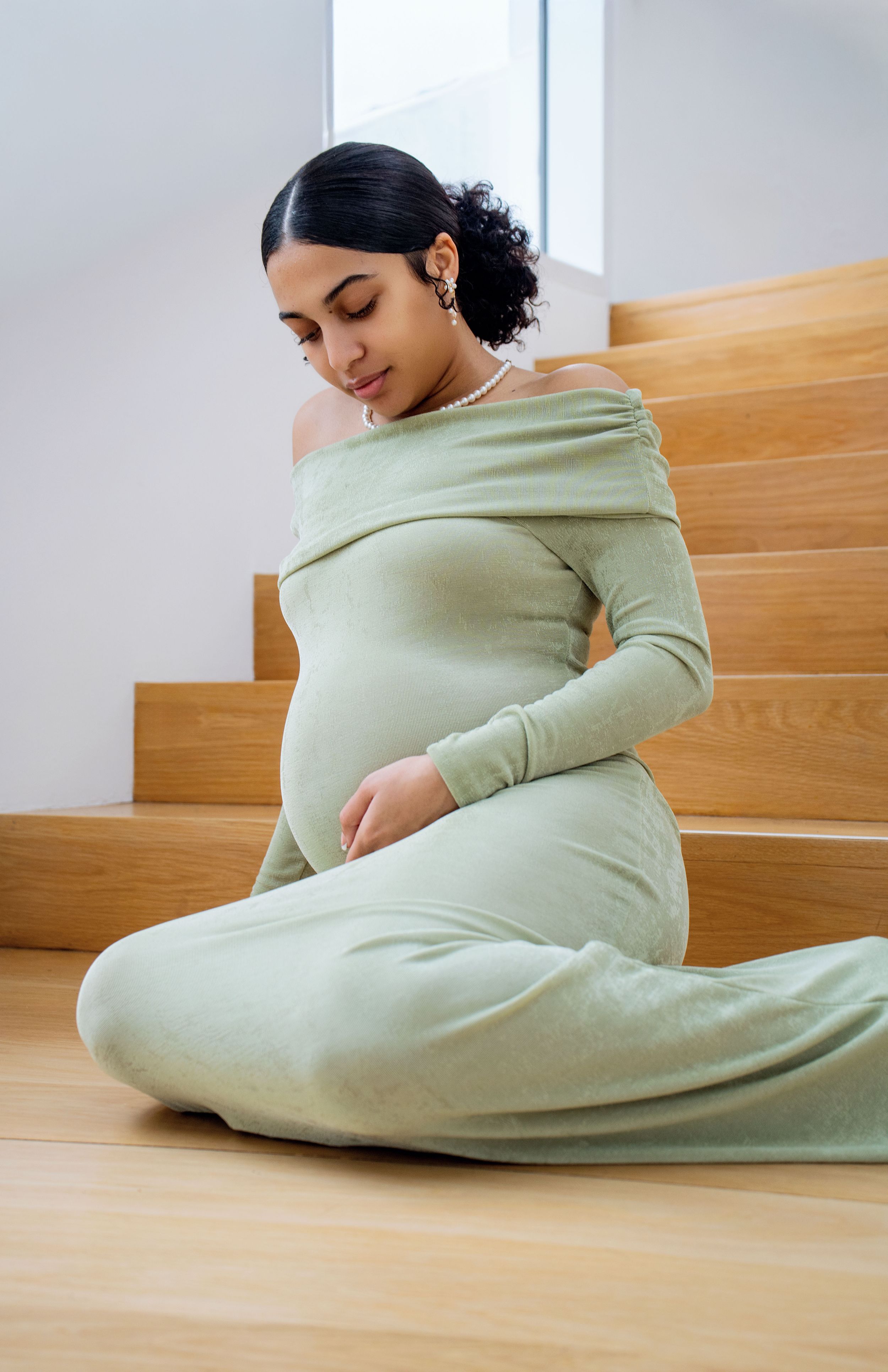 Person in mint green attire reclines gracefully on wooden stairs in an artistic pose.