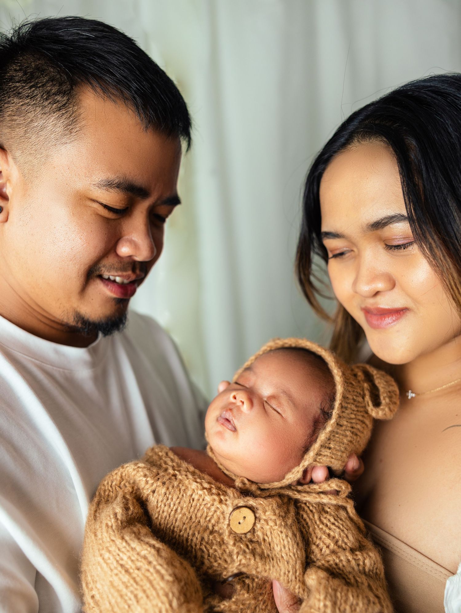 Young couple in casual attire tenderly holding their newborn baby wrapped in yellow knit.