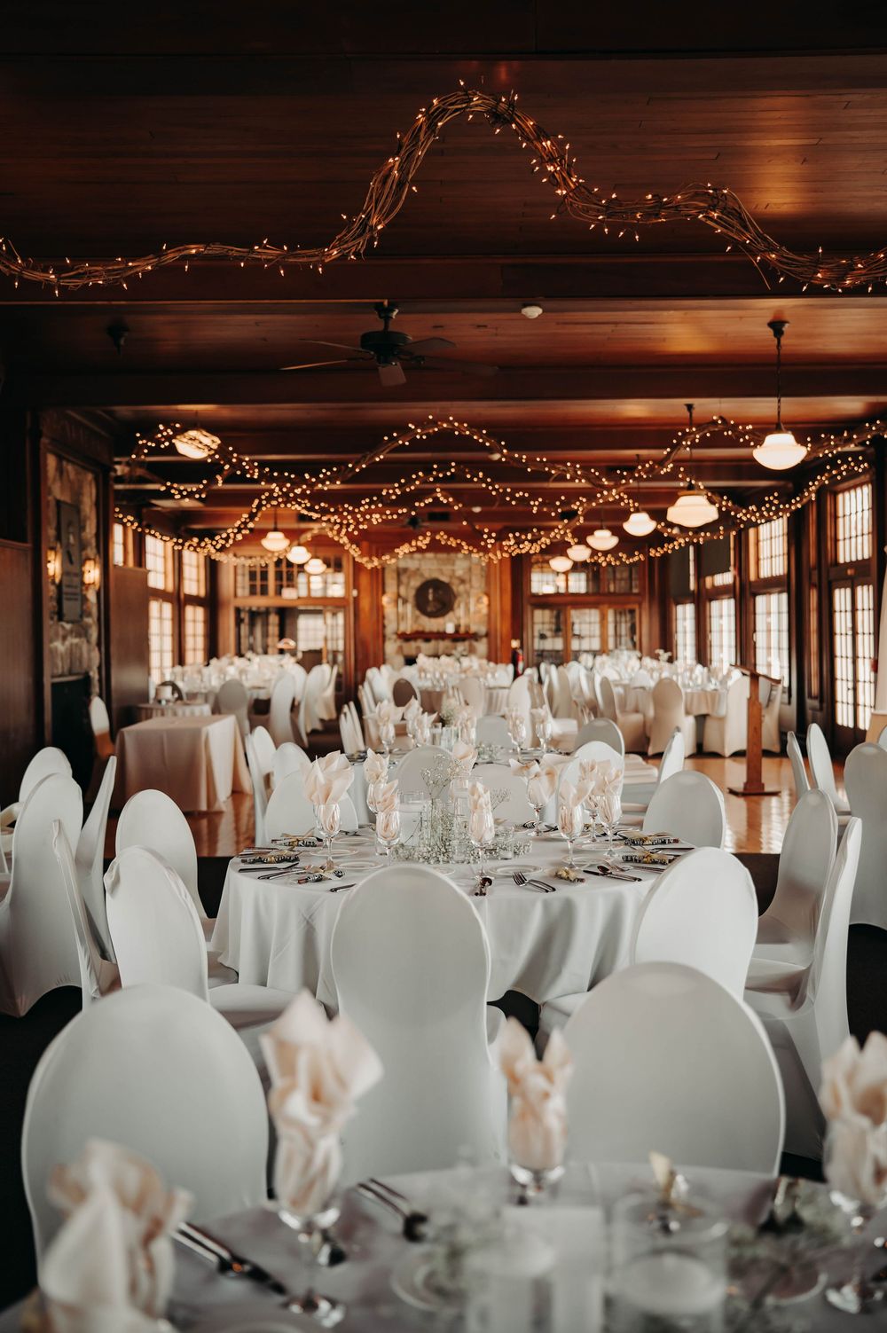 Elegant wedding reception hall with white round tables, chair covers, and warm string light decor.