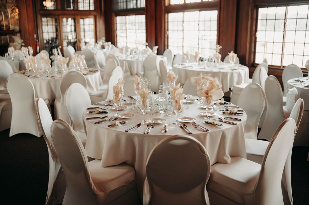Elegant wedding reception hall with round tables, white chair covers, and soft floral centerpieces in a warm wood-paneled venue.