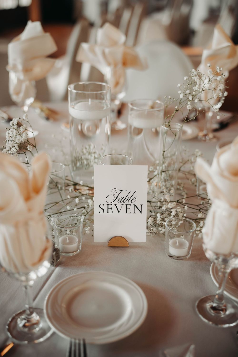 Wedding reception Table Seven place setting with baby's breath centerpieces, champagne flutes, and blush napkin folds.