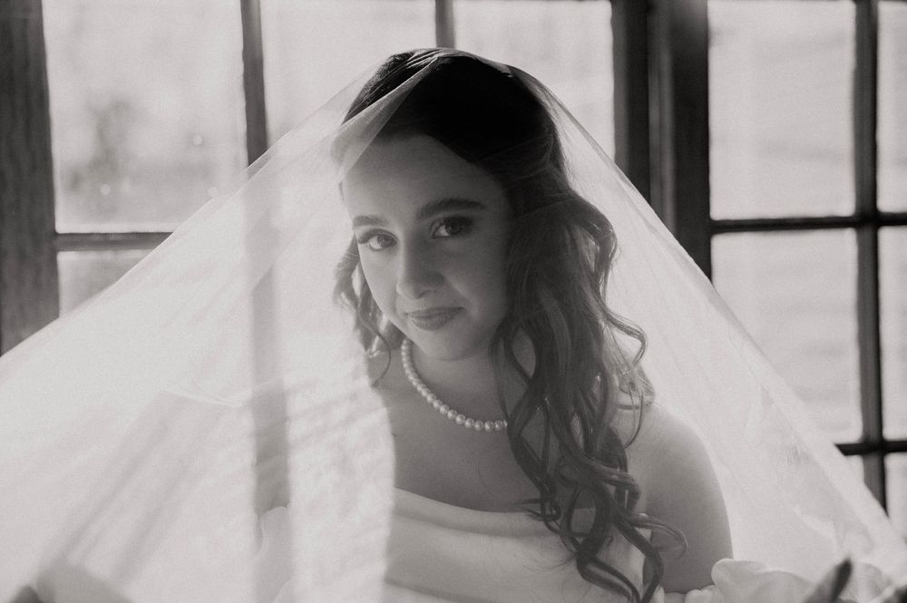 Black and white portrait of a bride wearing a pearl necklace draped under her flowing wedding veil.