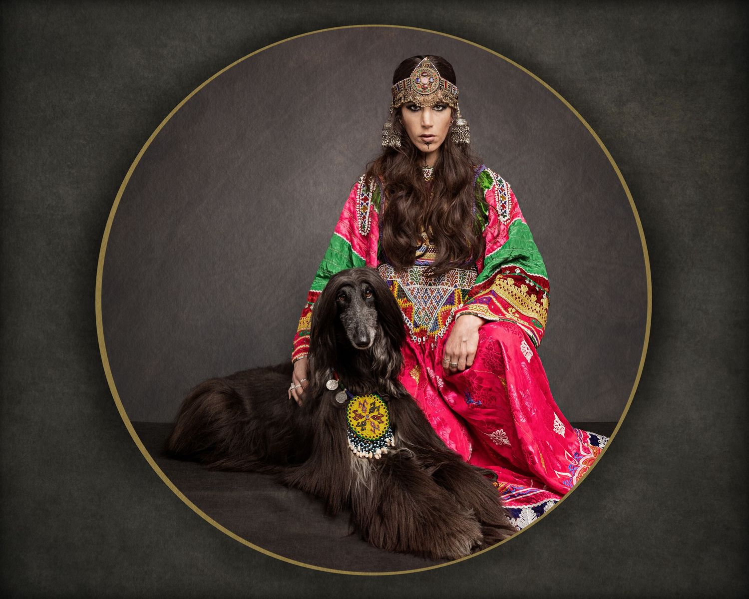 A figure in vibrant traditional dress sits with a black Afghan dog in a circular framed portrait against dark background.