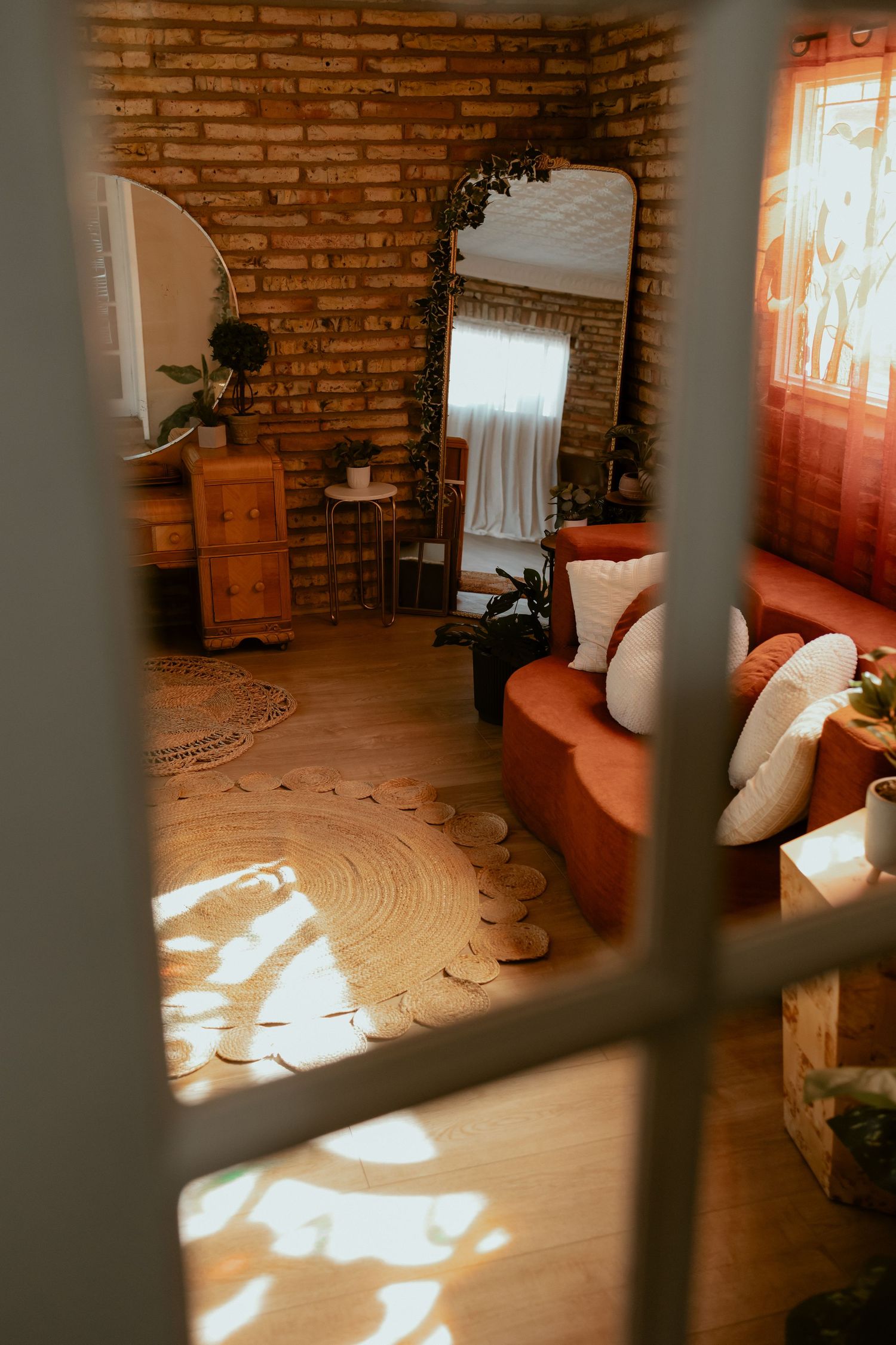 Cozy living room with exposed brick walls, curved seating, and warm sunlight streaming through window bars.