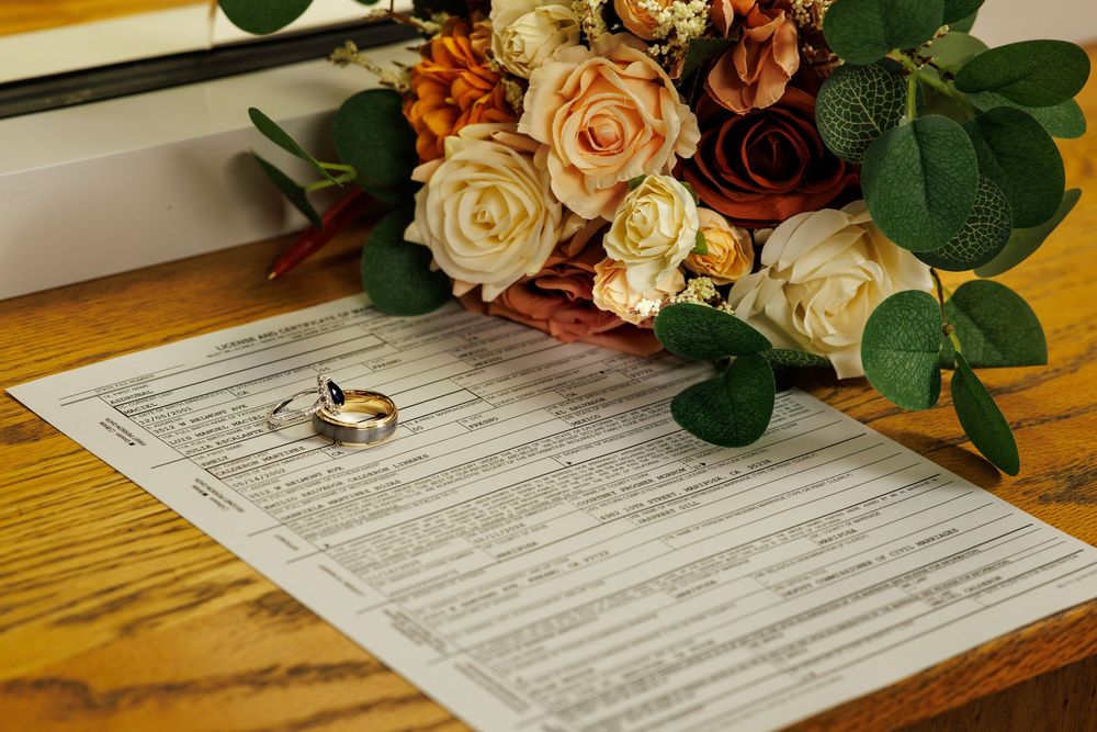 Wedding documents and floral arrangements displayed on wooden surface.