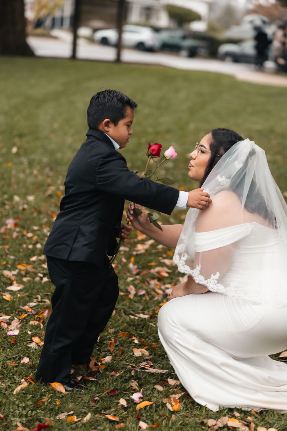 Young ring bearer presents a red rose to bride during outdoor wedding photos.