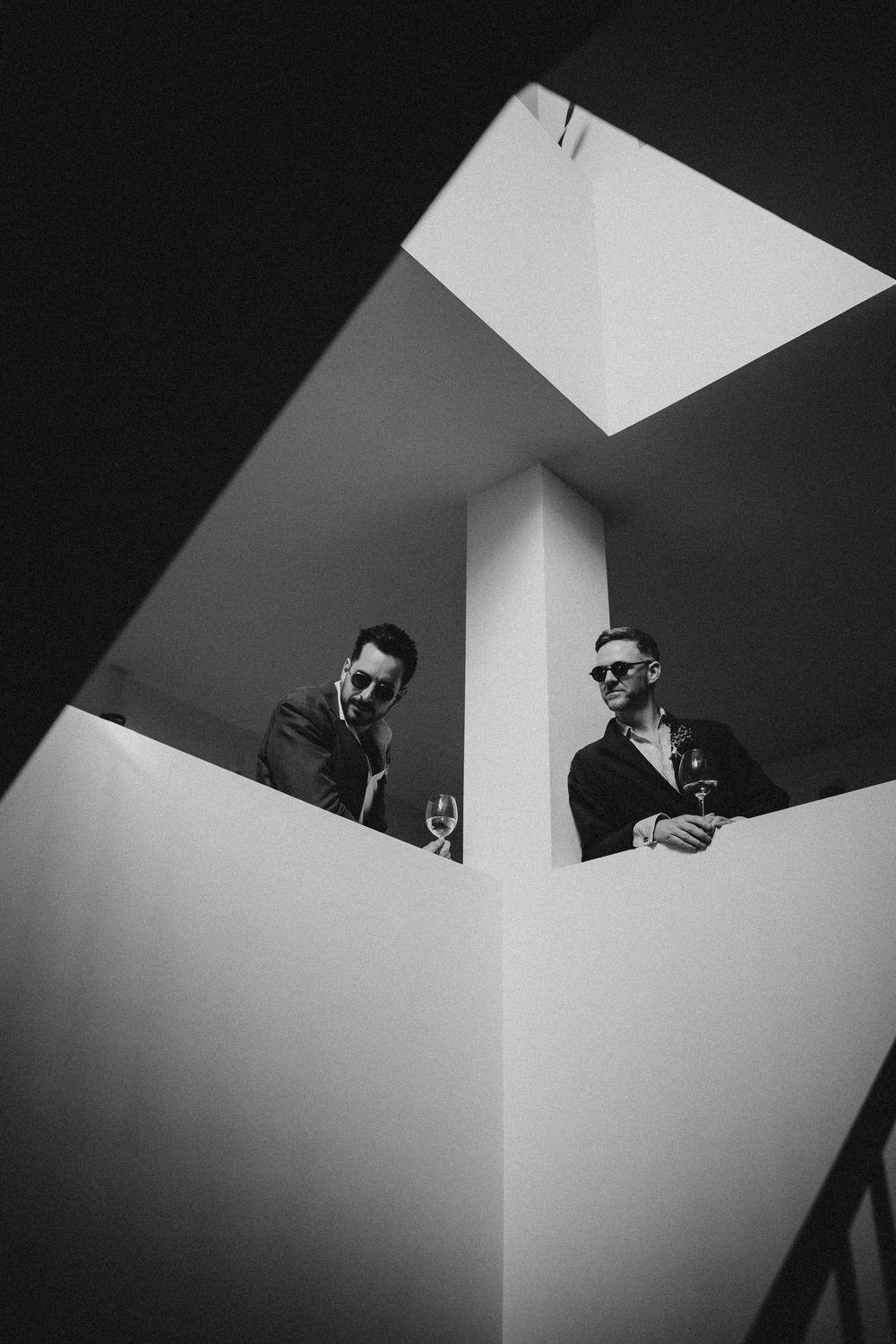 Black and white architectural photo showing two people standing in a geometric interior space with dramatic lighting.
