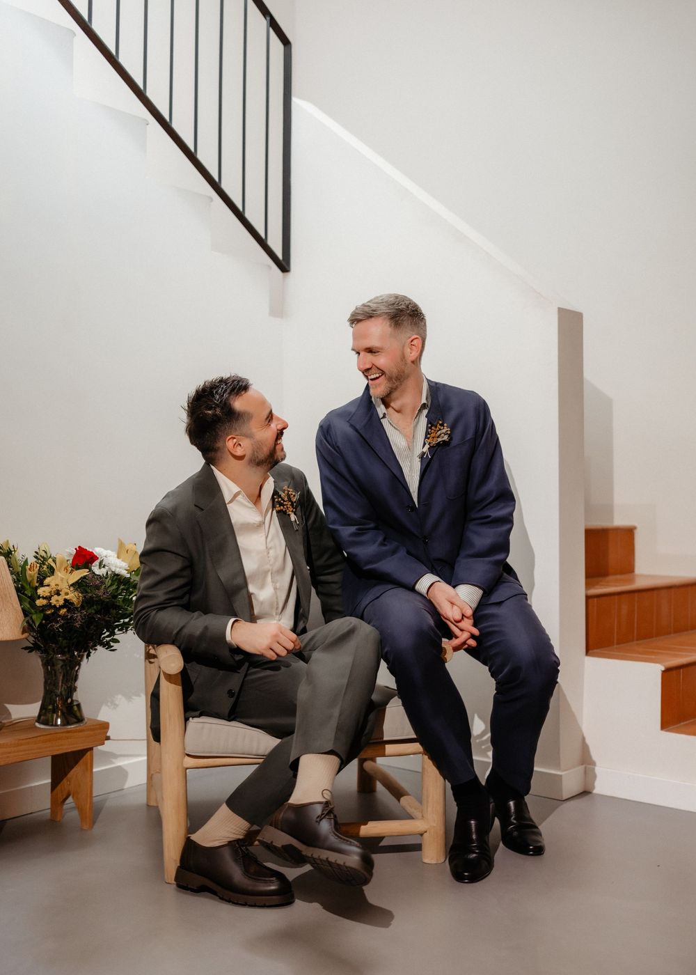 Two people sitting on a bench engage in conversation with a vase of red roses visible in the background.