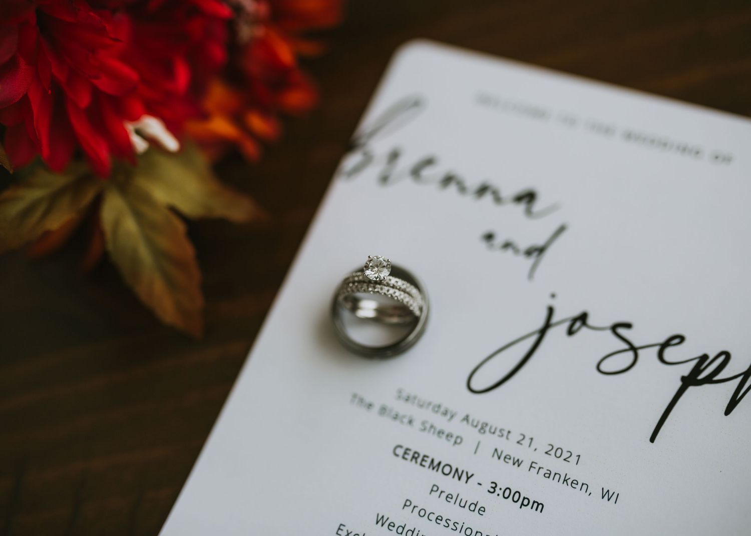 Wedding rings and invitation details with red autumn foliage accents.