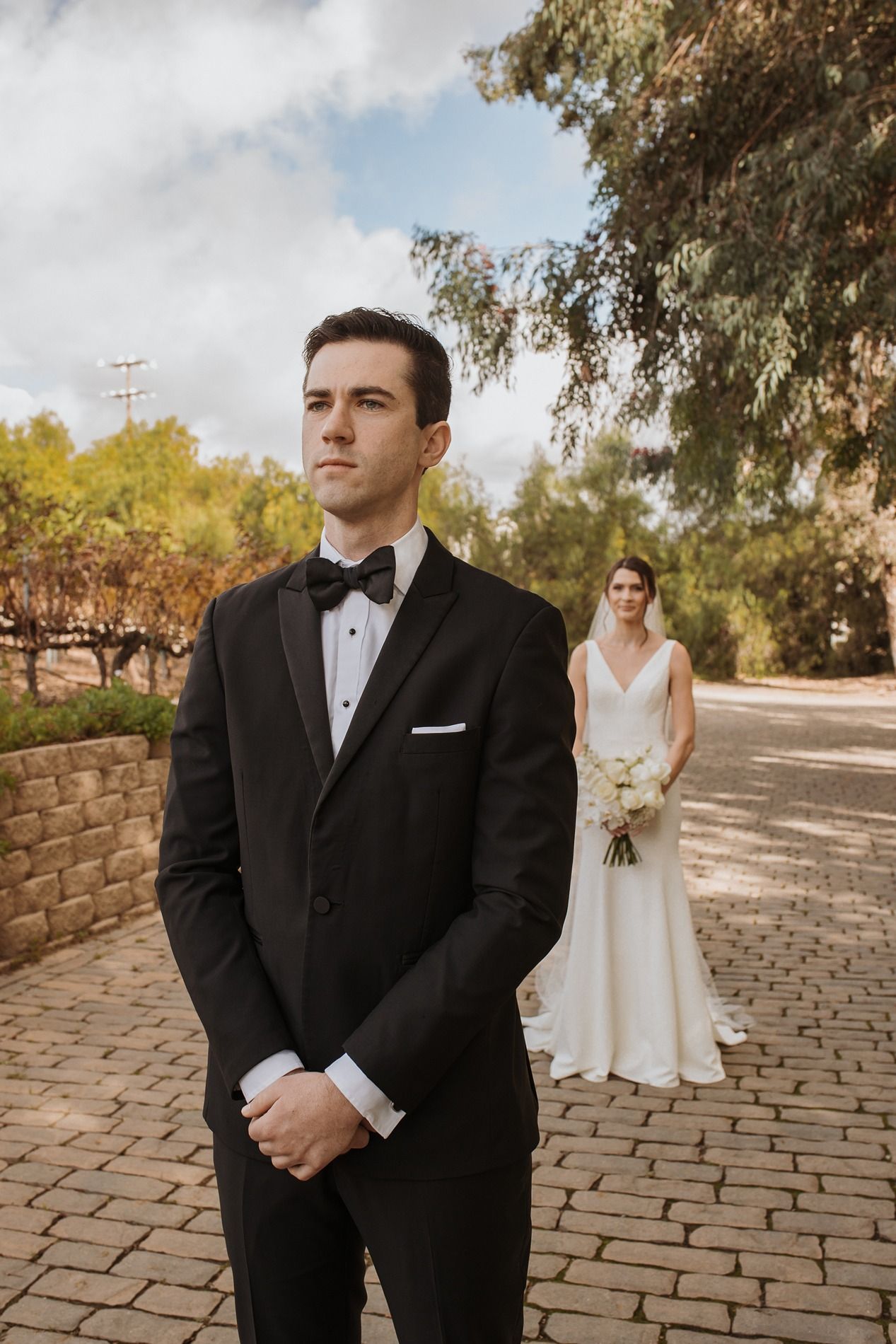 A wedding first look moment captured on a stone path surrounded by lush greenery on a sunny day at Lake Oak Meadows in Temecula.