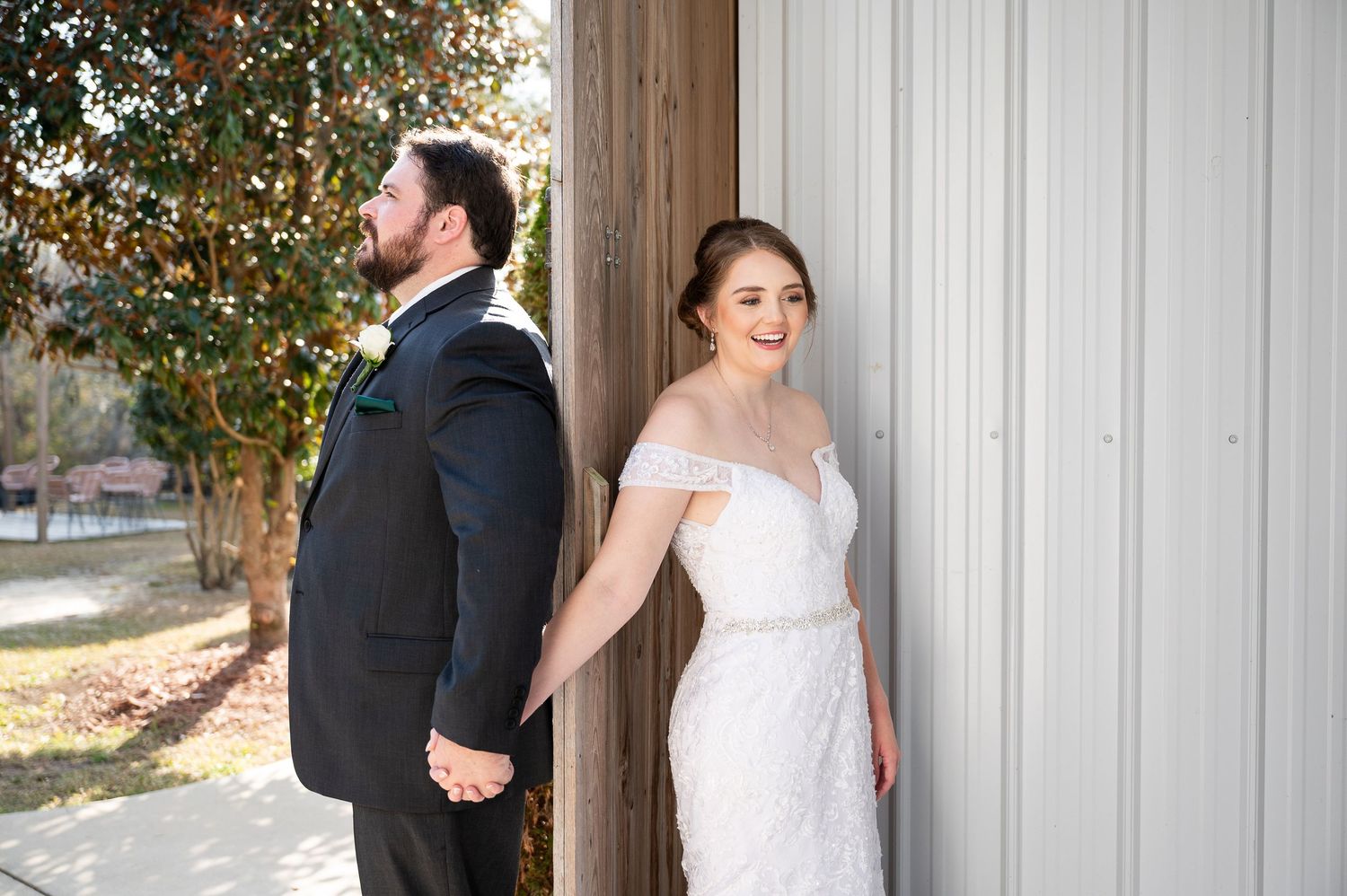 Wedding couple poses against white barn wall with decorative greenery.