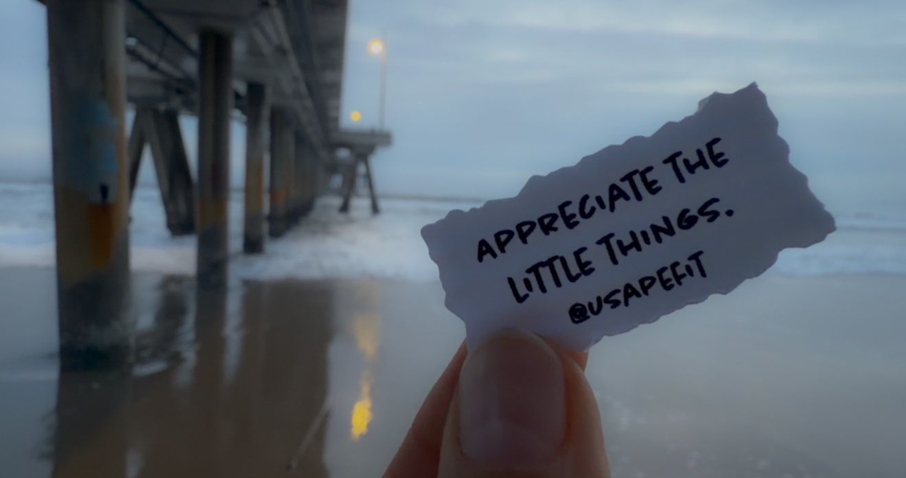 A hand holds up a small handwritten note against a blurry outdoor background.