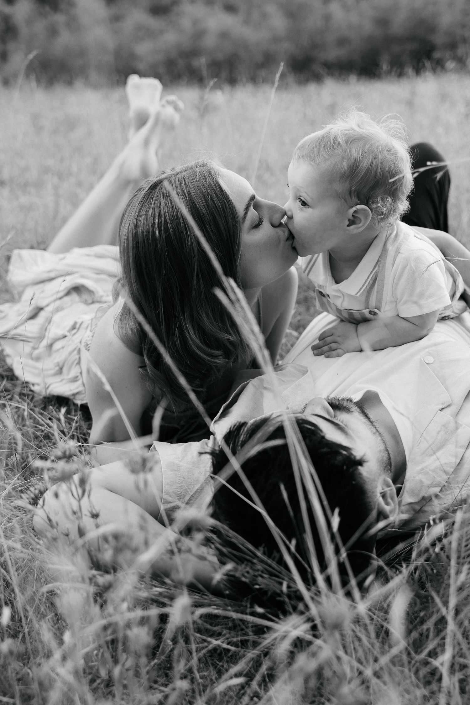 A tender black and white photo series showing intimate moments between parent and child lying in tall grass.