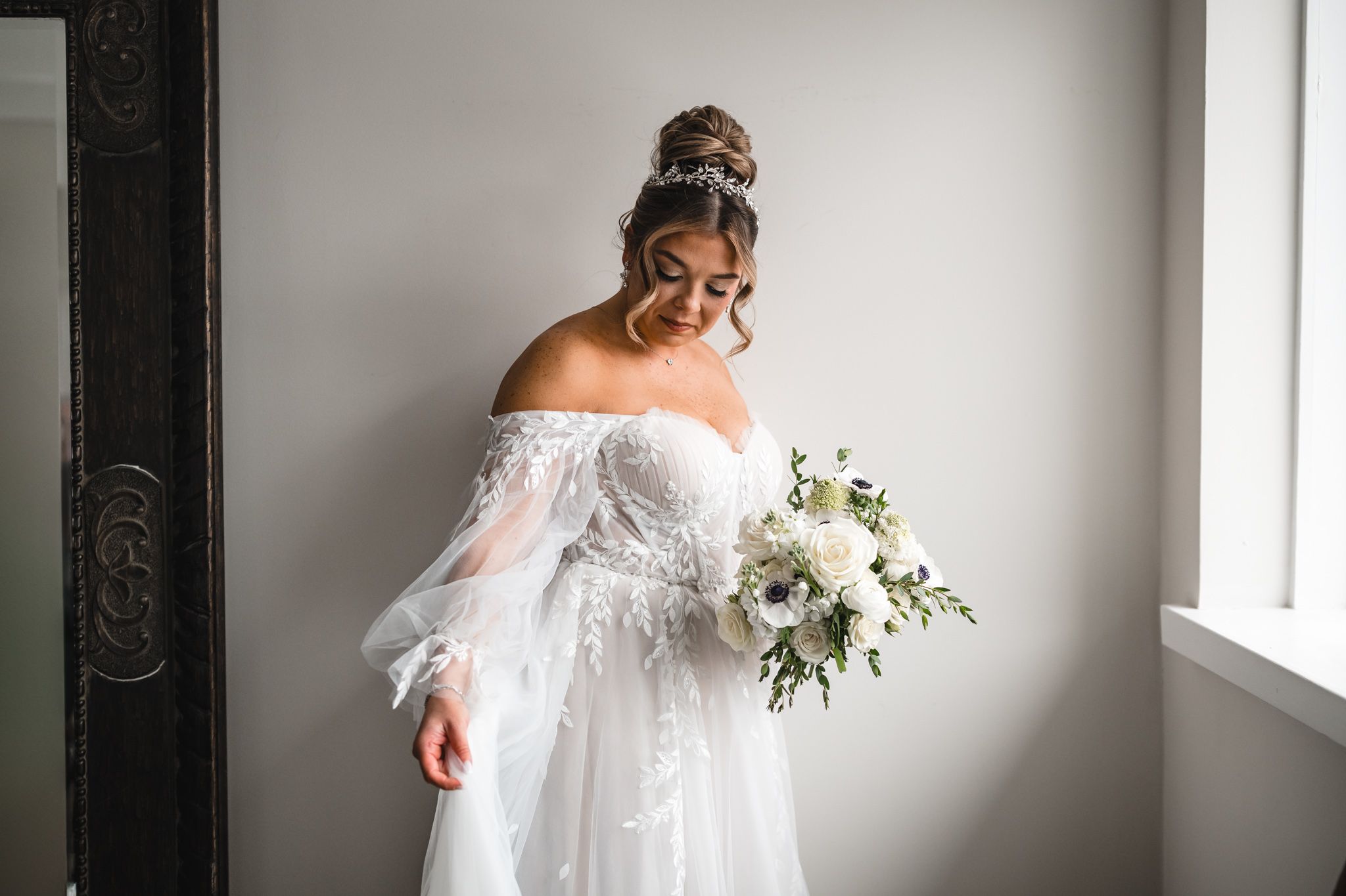 Ethereal bridal portraits near window with white bouquet and flowing dress.