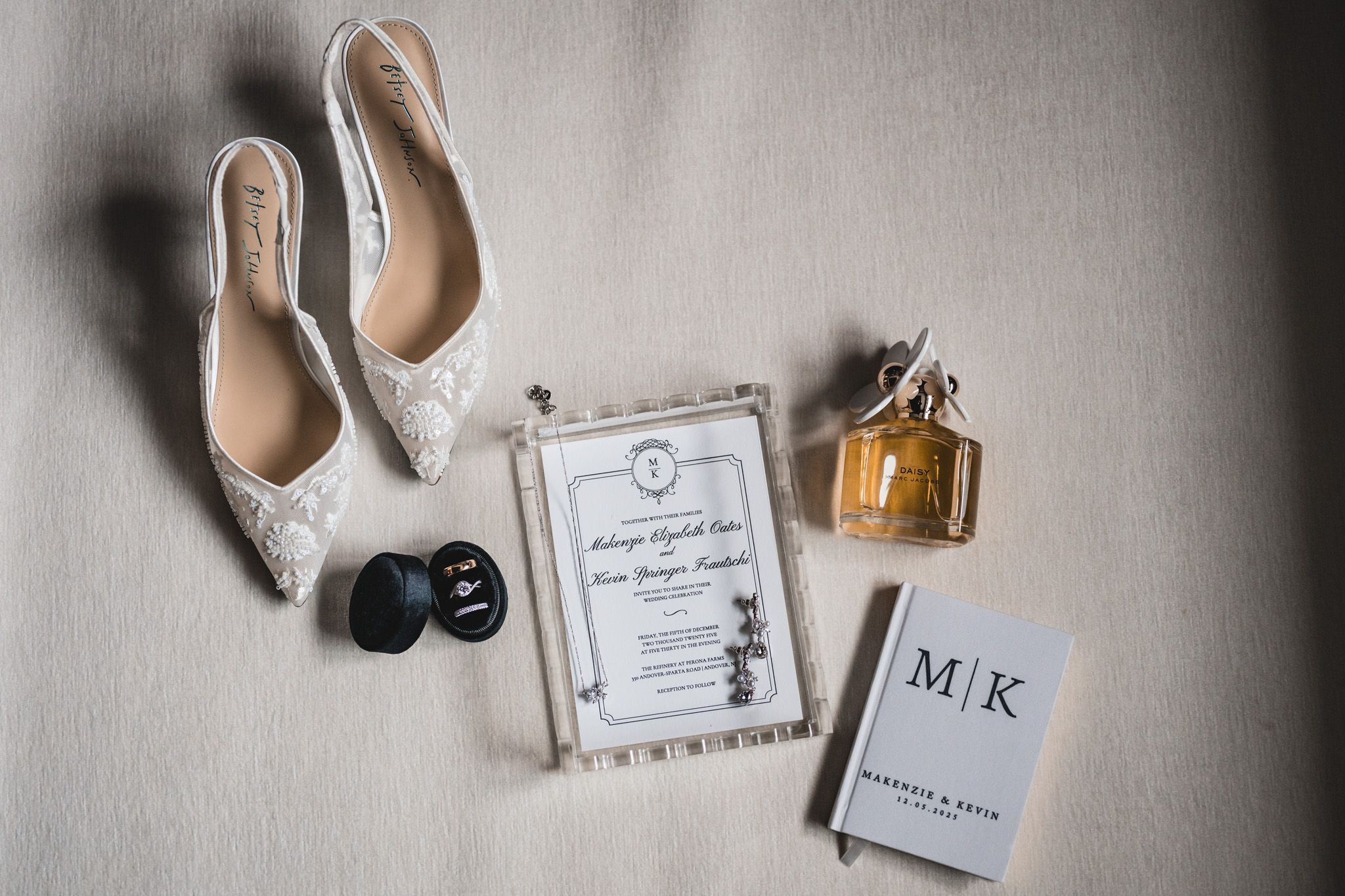 Wedding details flatlay with lace shoes, invitation, perfume and monogrammed items.