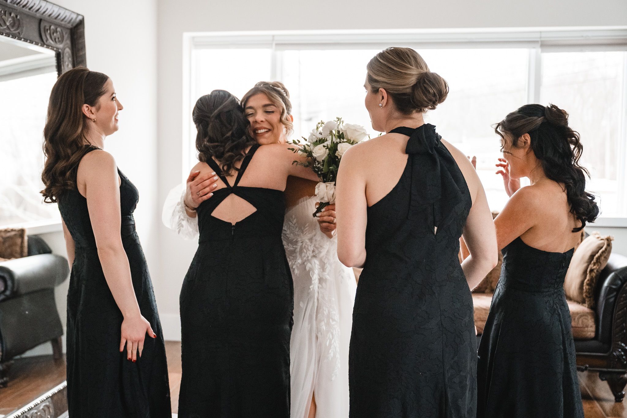 Wedding party wearing elegant black dresses pose together in a bright indoor setting.
