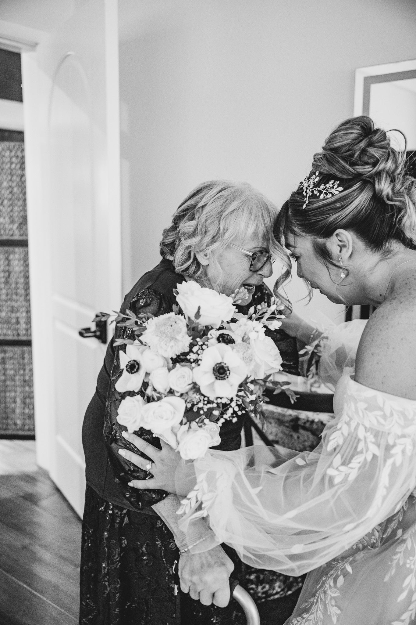 An emotional moment shared between a bride and elderly woman holding a bouquet of white flowers.