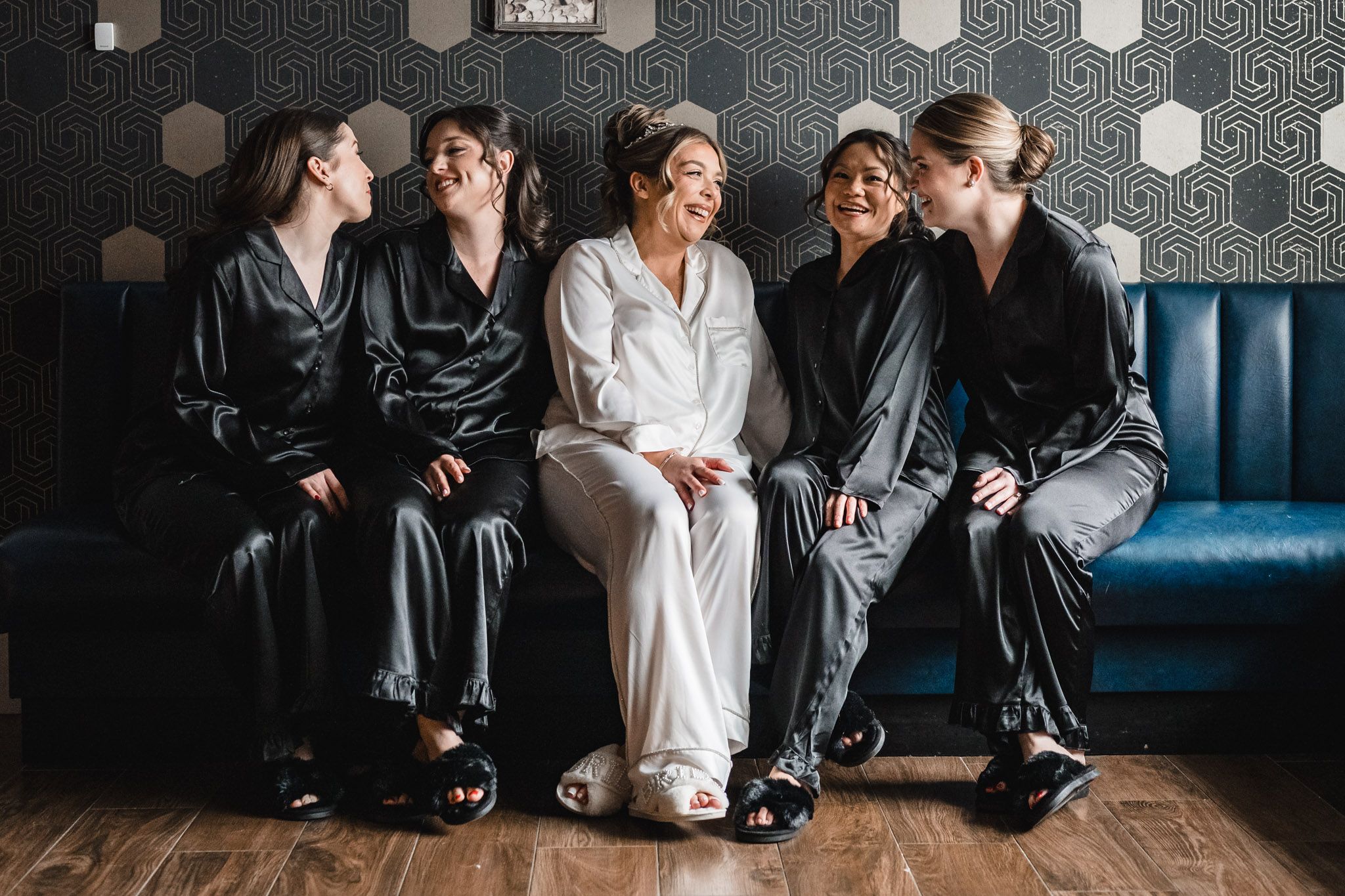 Wedding party seated on a blue velvet couch sharing candid laughs and smiles.