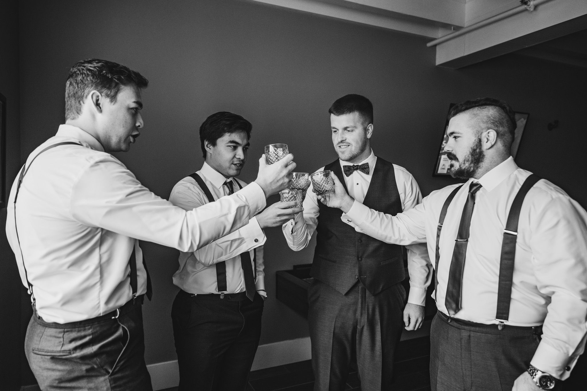 Groomsmen in white shirts and suspenders sharing celebratory drinks together.