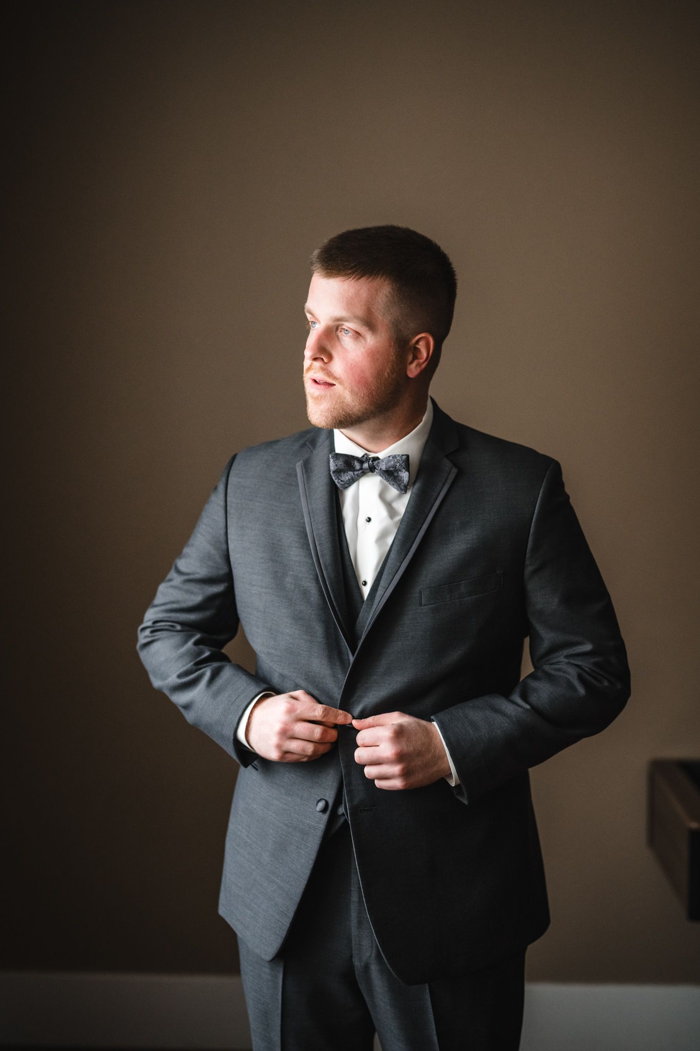 A groom in a classic black tuxedo and bow tie poses against a dark background.