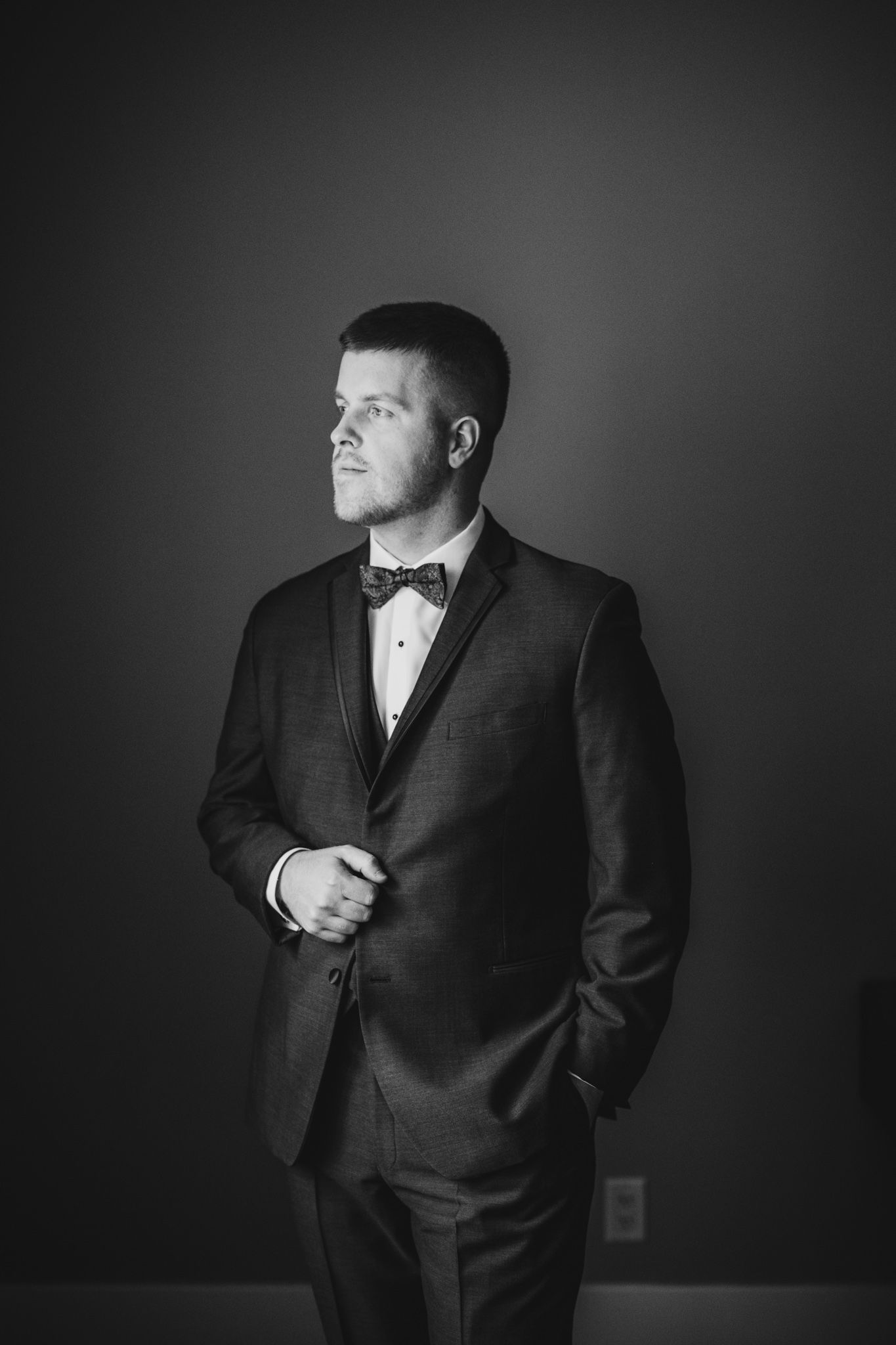 A dramatic black and white portrait of a groom in formal attire against a dark backdrop.