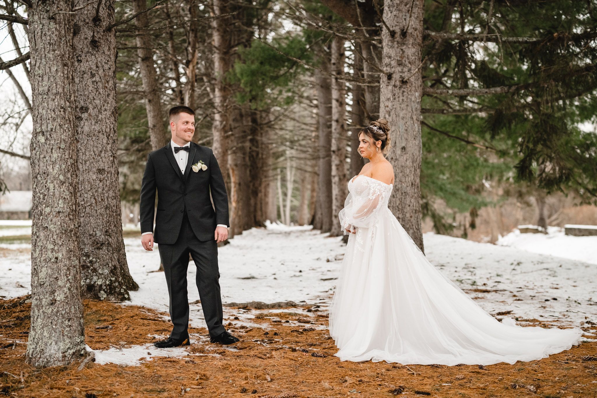 Winter wedding couple poses among snow-covered trees in forest setting.