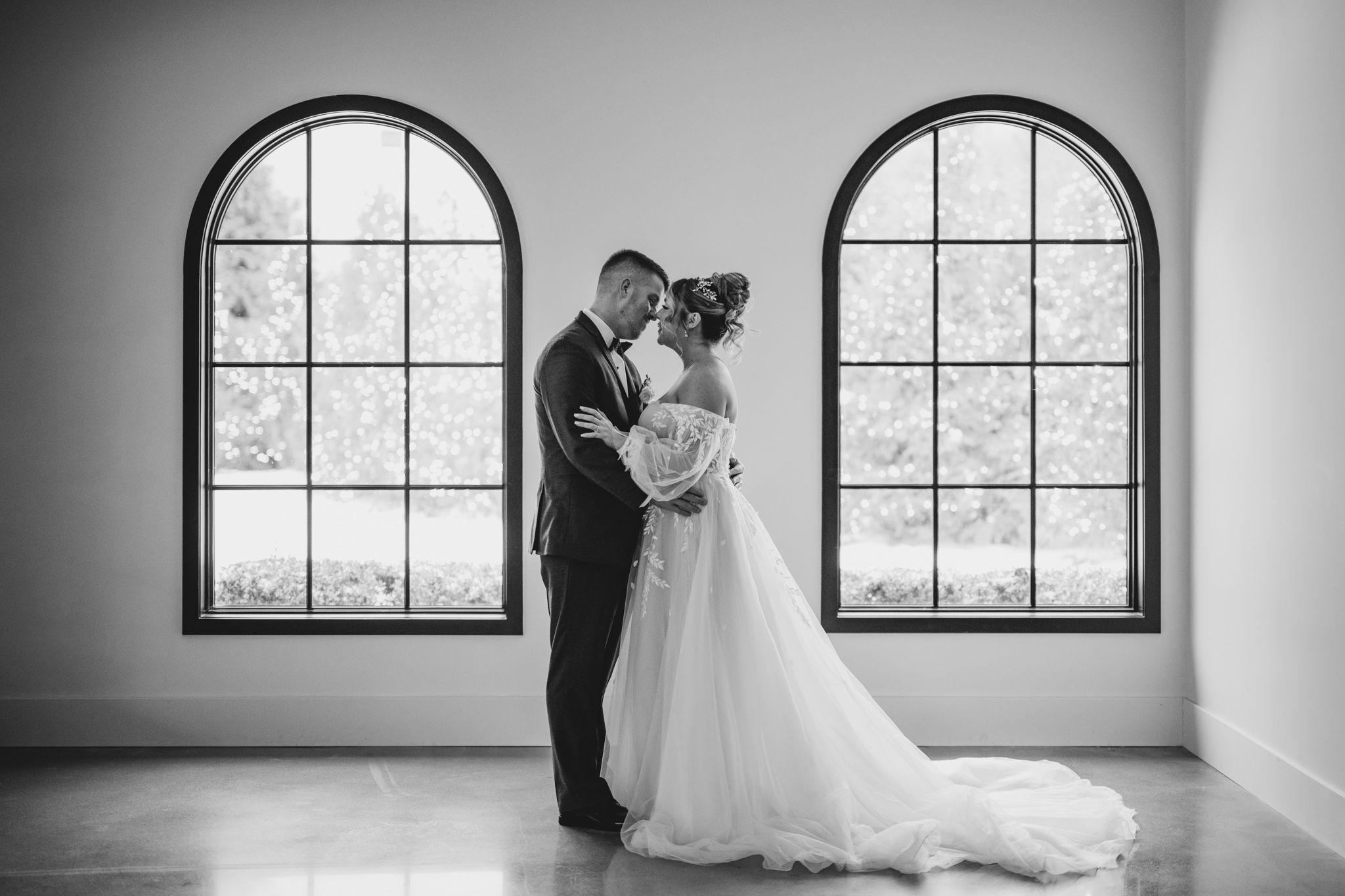A black and white wedding portrait with arched windows creating dramatic natural lighting.