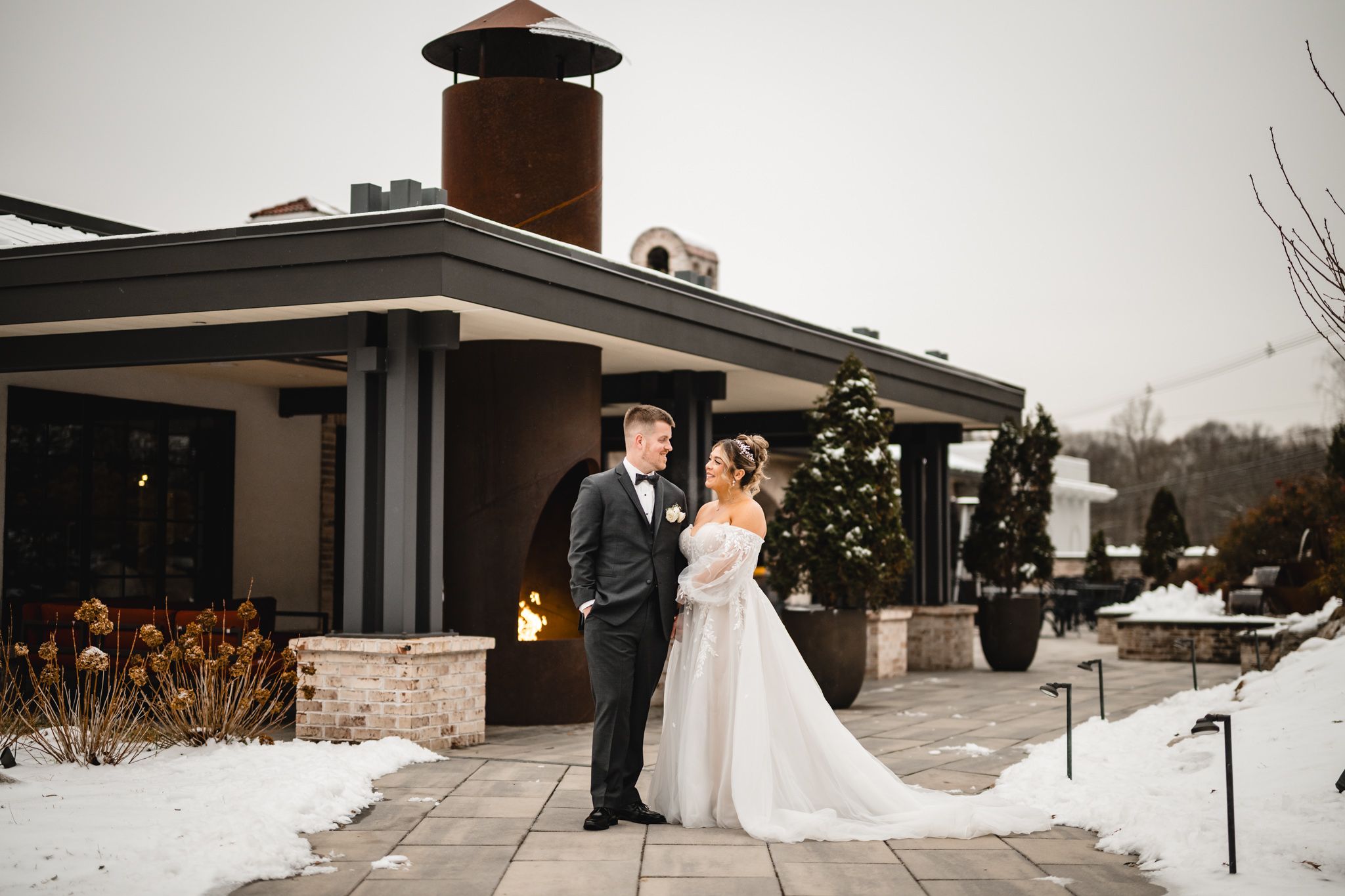 A winter wedding photo outside a venue with snow on the ground and a decorated Christmas tree.